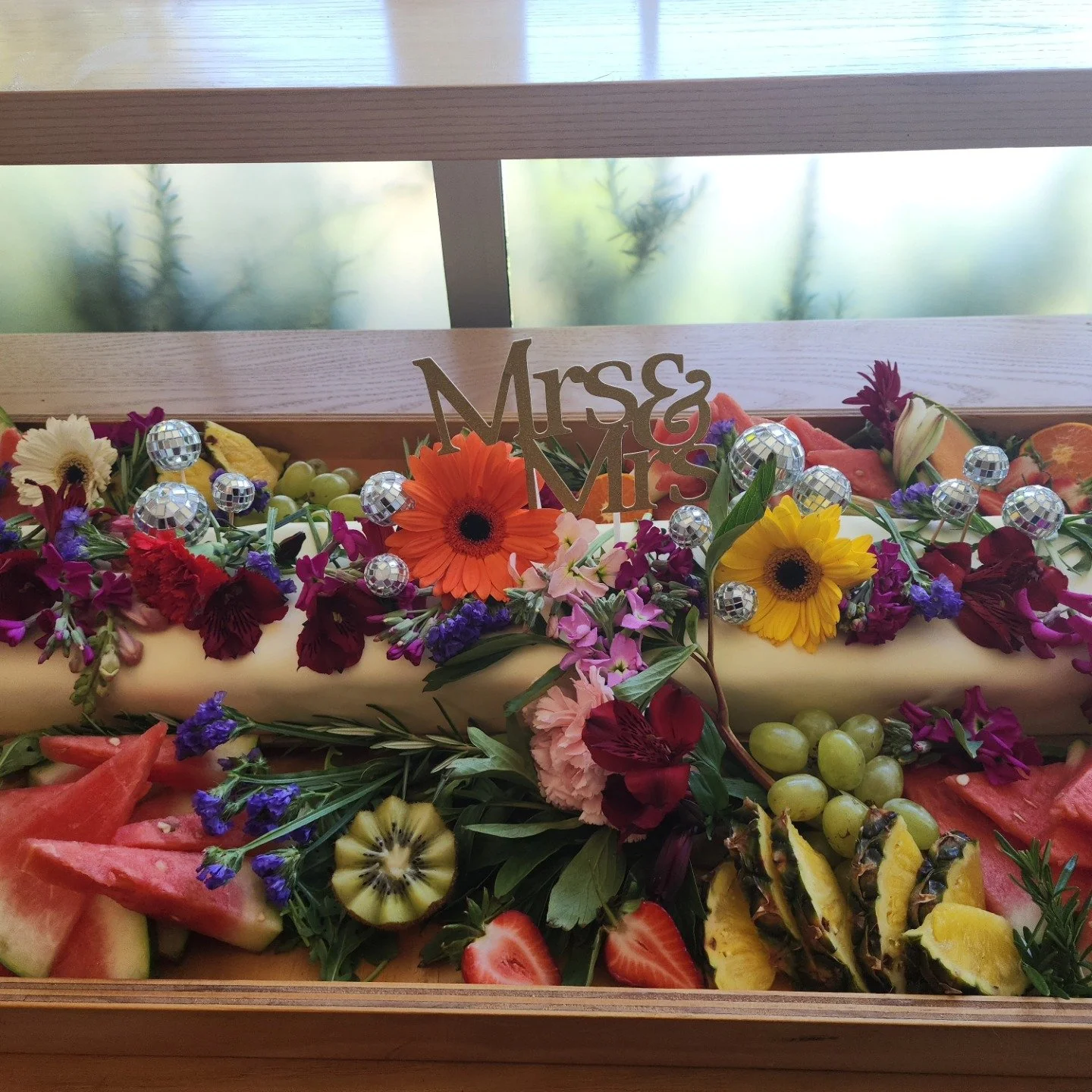 A decorative wedding display with a variety of colorful flowers, fresh fruits, small disco balls, and a 