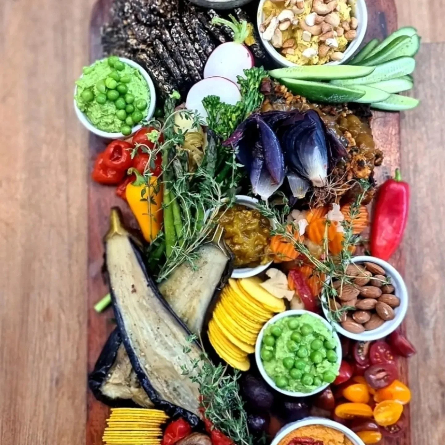 An assortment of fresh vegetables, fruits, fish, nuts, and herbs arranged on a large wooden platter.