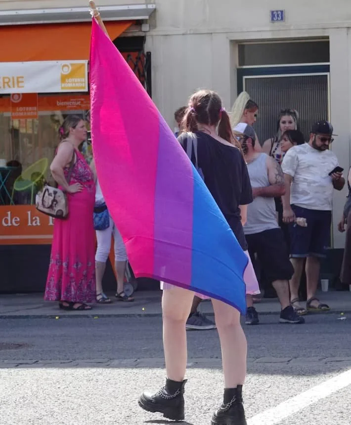 Person wrapped in a bisexual pride flag standing at a Pride event, representing visibility, identity, and belonging.