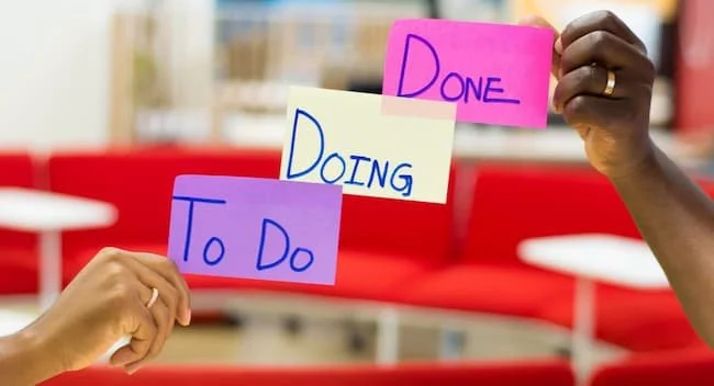 Hands holding colorful sticky notes labeled "To Do," "Doing," and "Done," illustrating productivity and task completion.