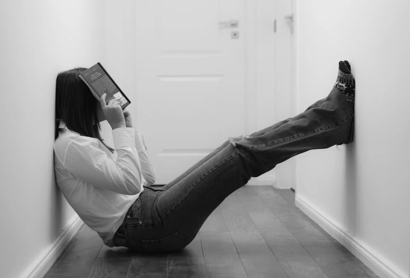 Person sitting on the floor with a book covering their face, suggesting emotional exhaustion and burnout.