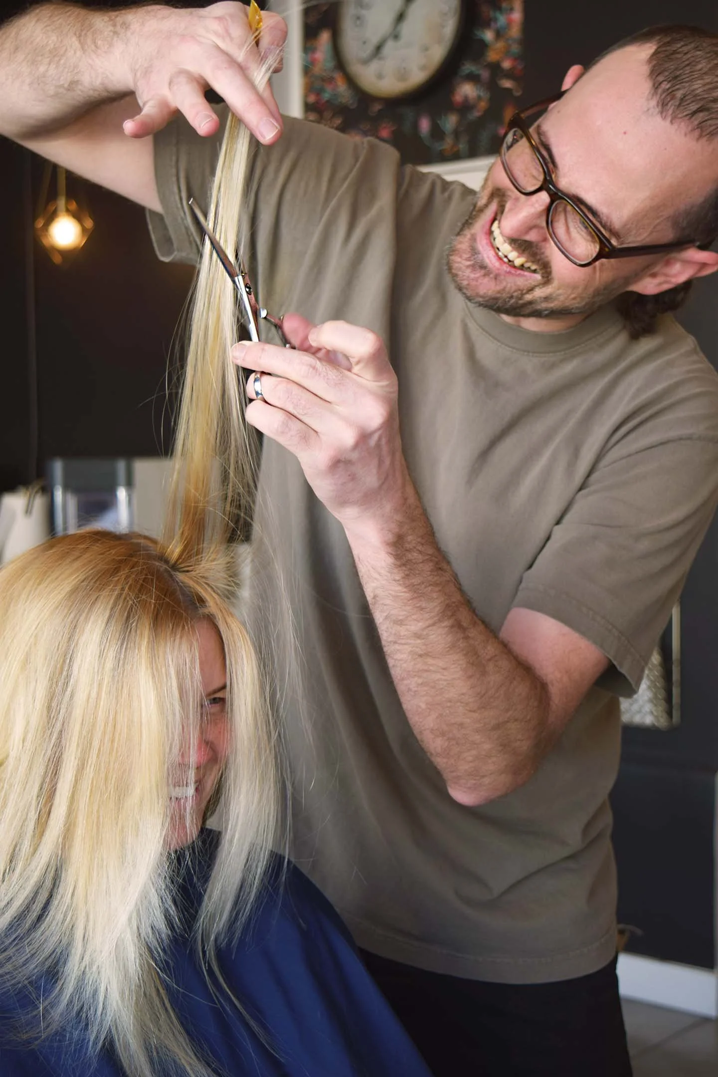 A hairstylist cutting a woman's long blonde hair in a salon.