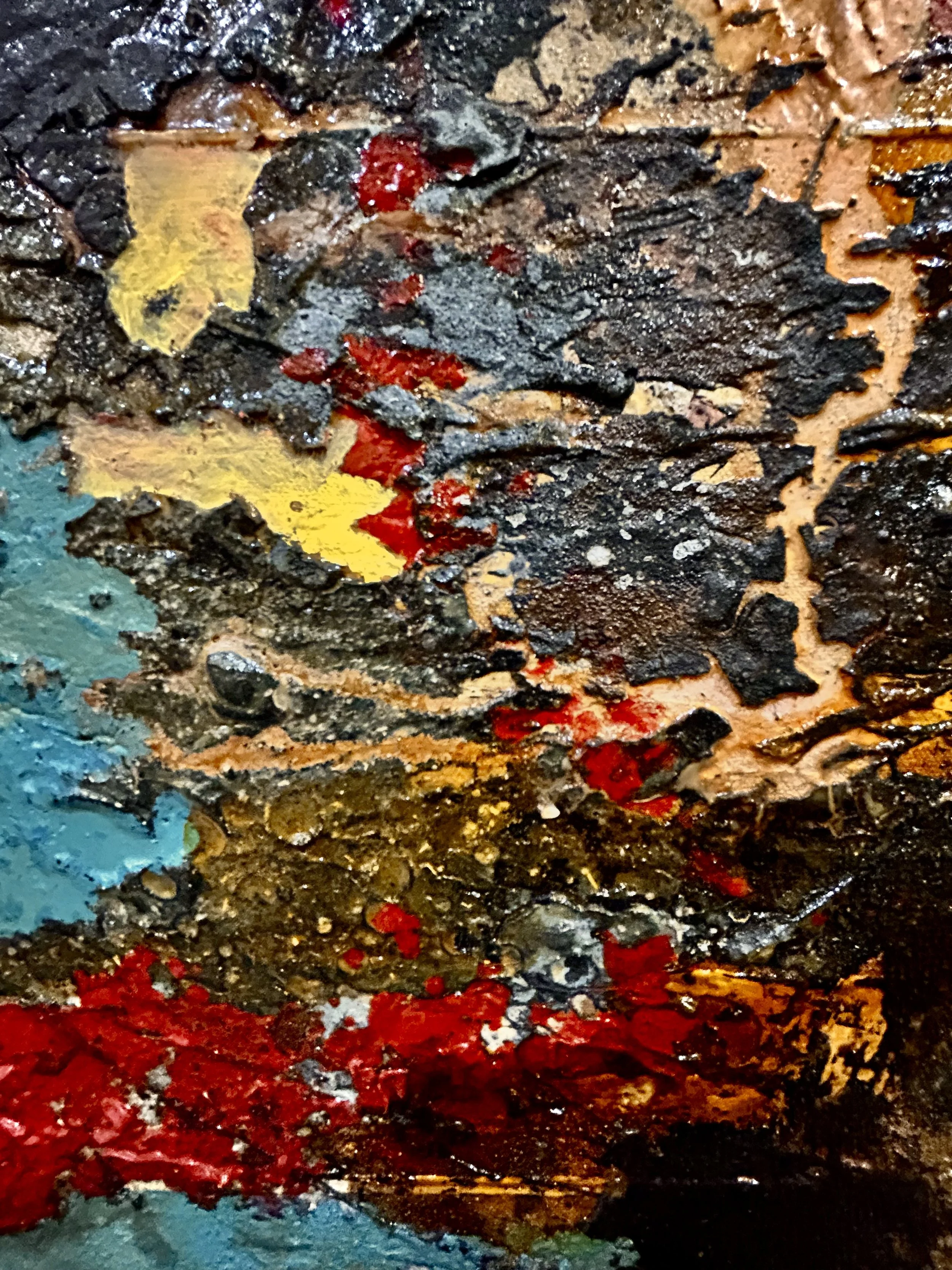 Close-up of a textured abstract painting with layers of dark, red, yellow, and blue paint, creating a rough, crackled surface with a variety of colors blending together.