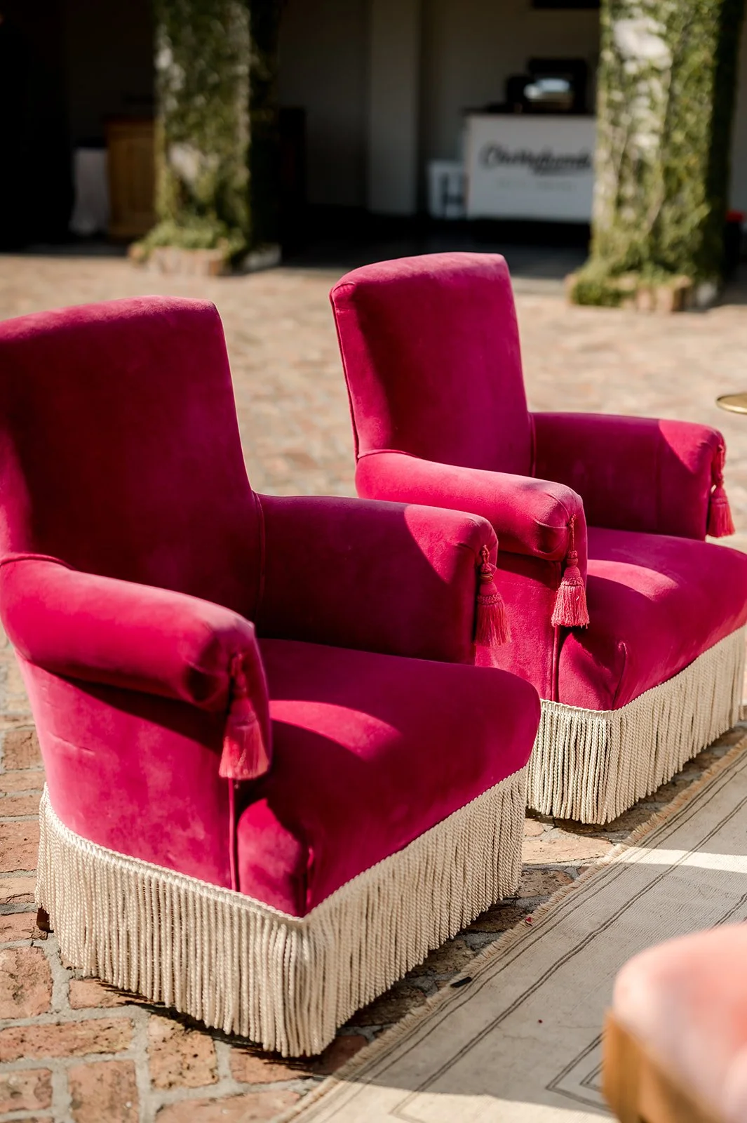 Two vintage pink velvet armchairs with tassel trim sitting on a brick patio.