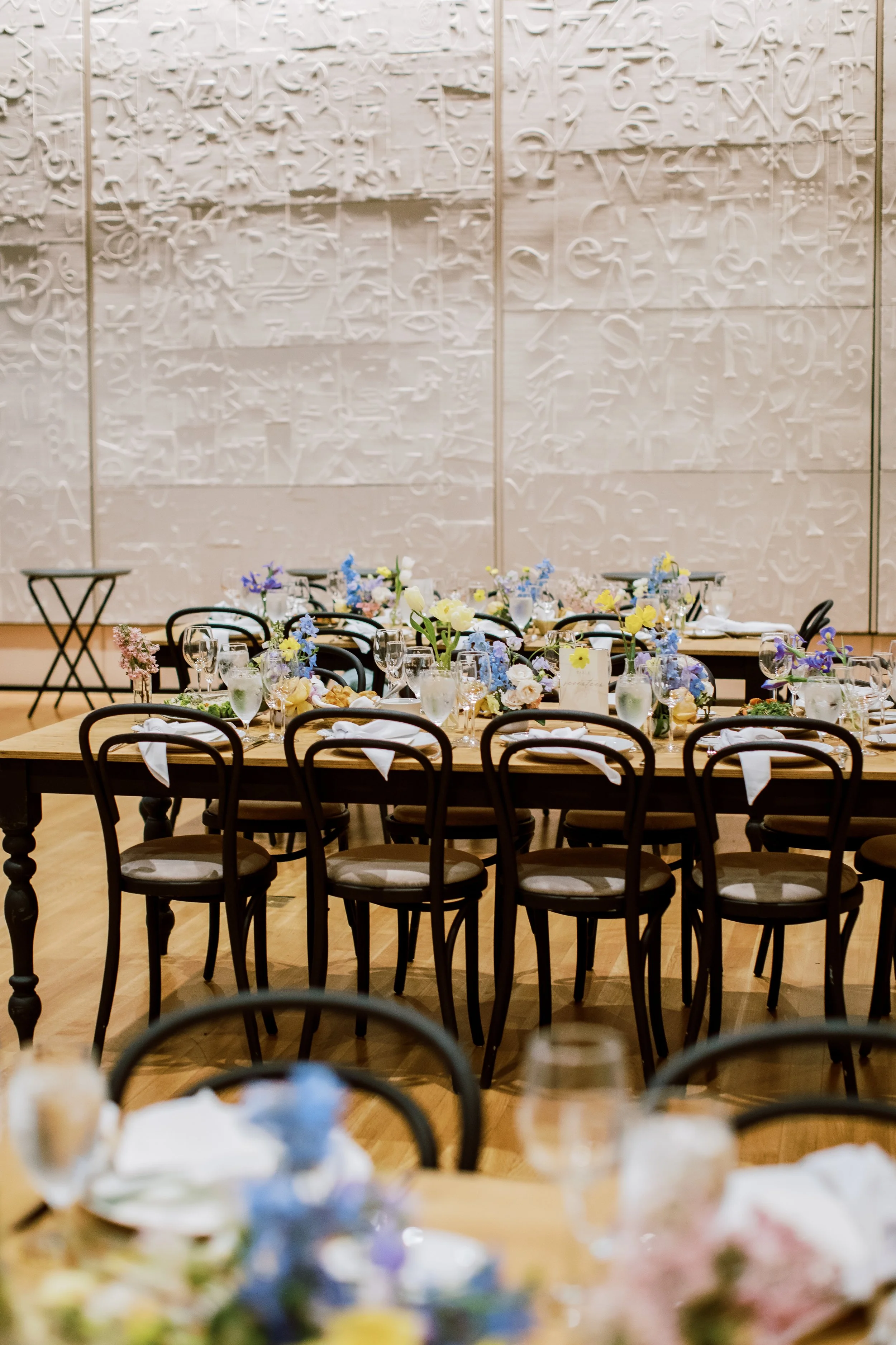 A banquet hall with decorated tables and chairs, set for a formal event, with a textured white wall in the background.