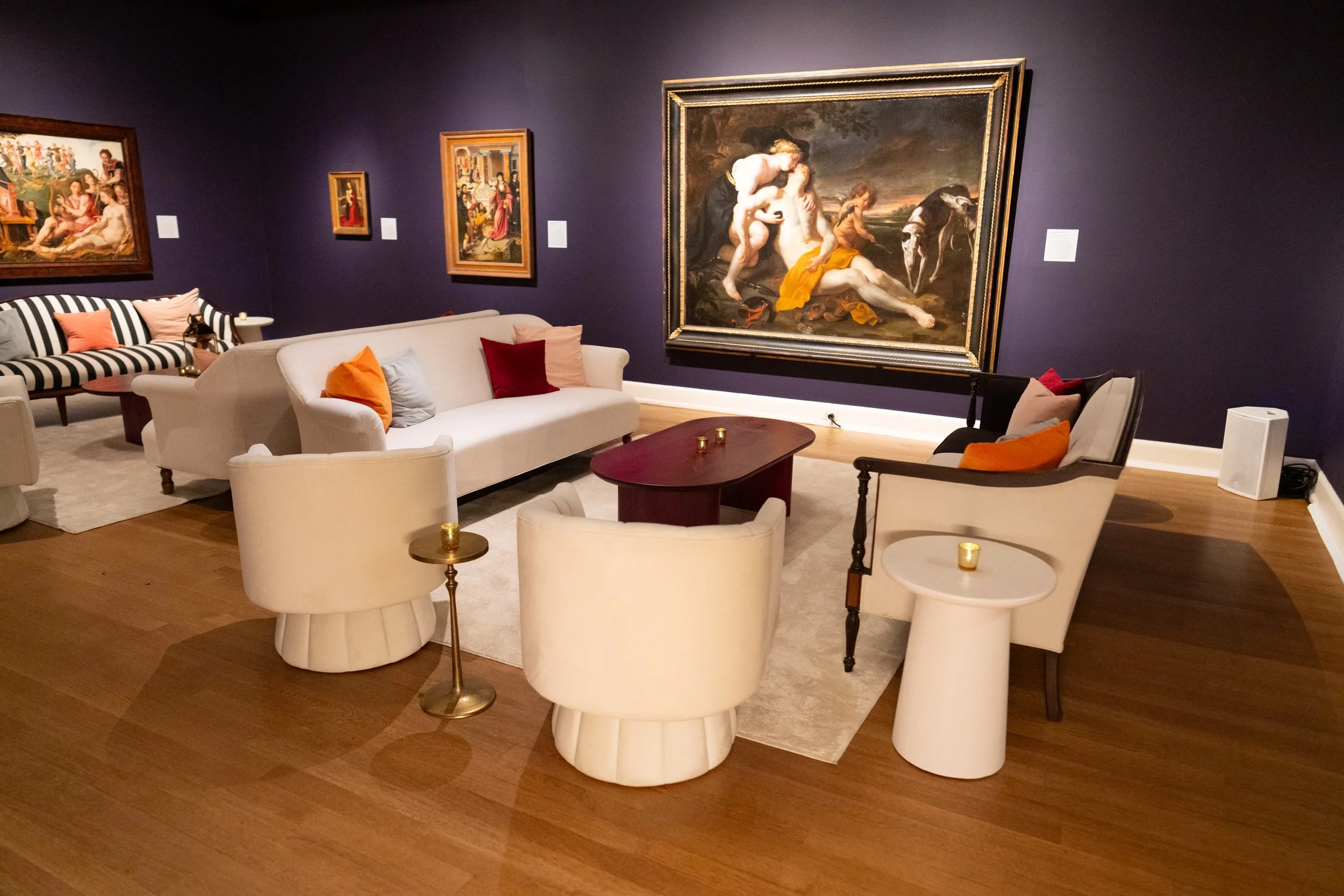 Living room with purple walls, white and patterned furniture, and classical paintings on the walls.