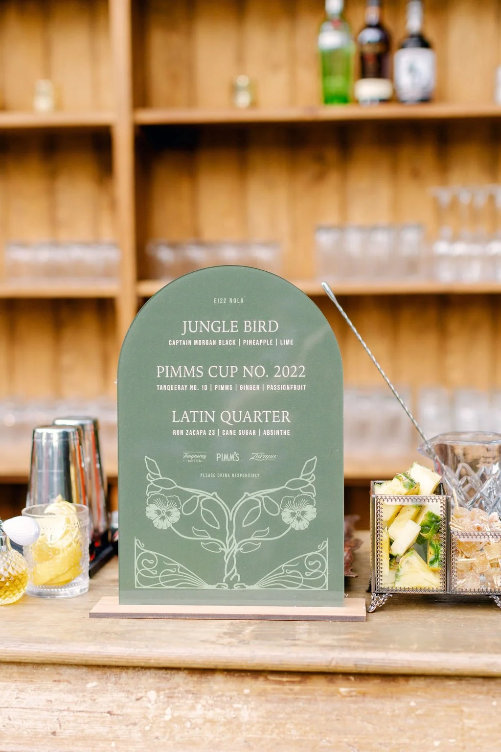 A green drink menu sign listing three cocktail options: Jungle Bird with Captain Morgan Black, pineapple, and lime; Pimm's Cup No. 202 with Tanqueray No. 10, Pimm's, ginger, and passionfruit; Latin Quarter with Ron Zacapa 23, cane sugar, and absinthe