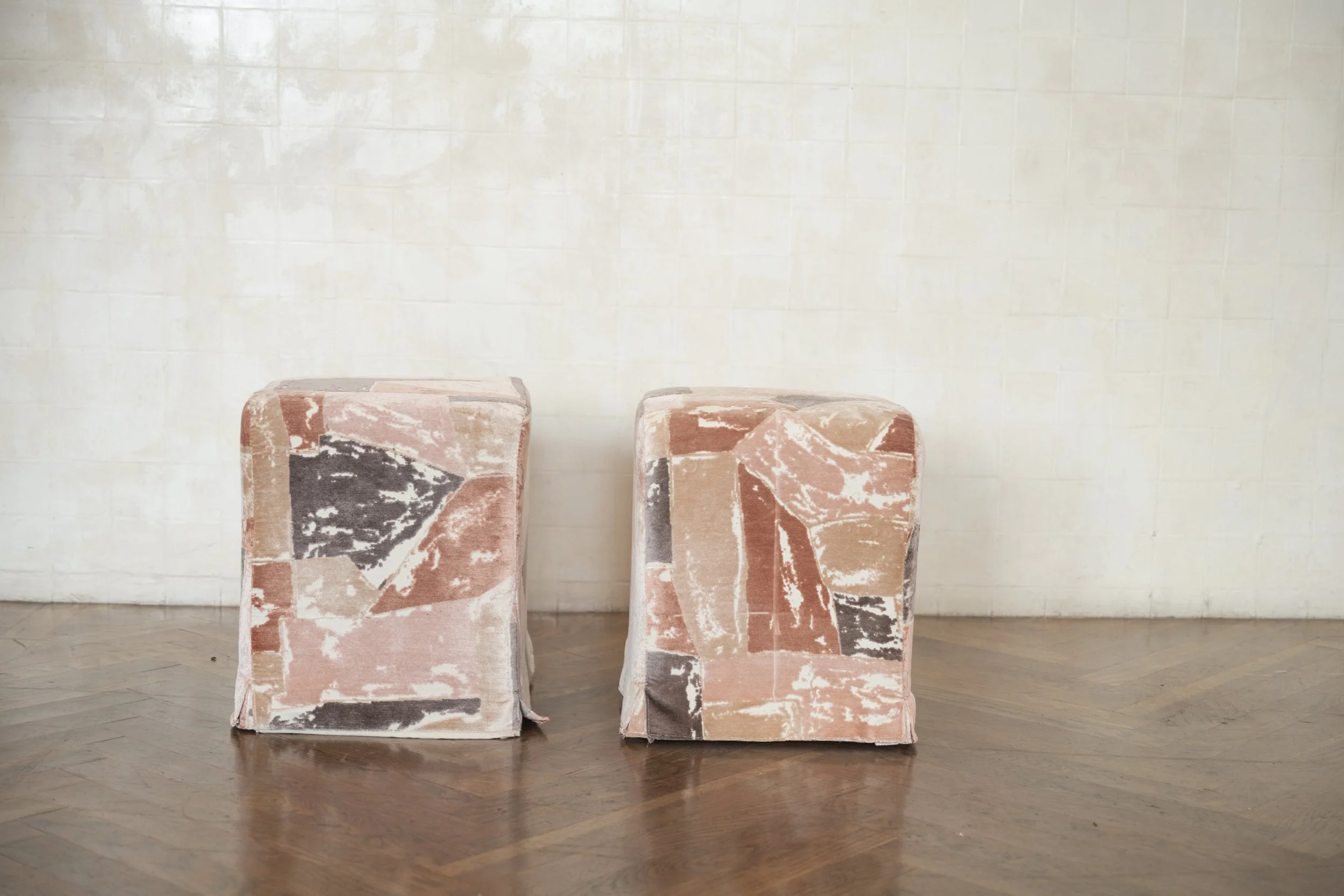 Two upholstered chairs with geometric and marble pattern fabric, placed side by side against a white tiled wall.