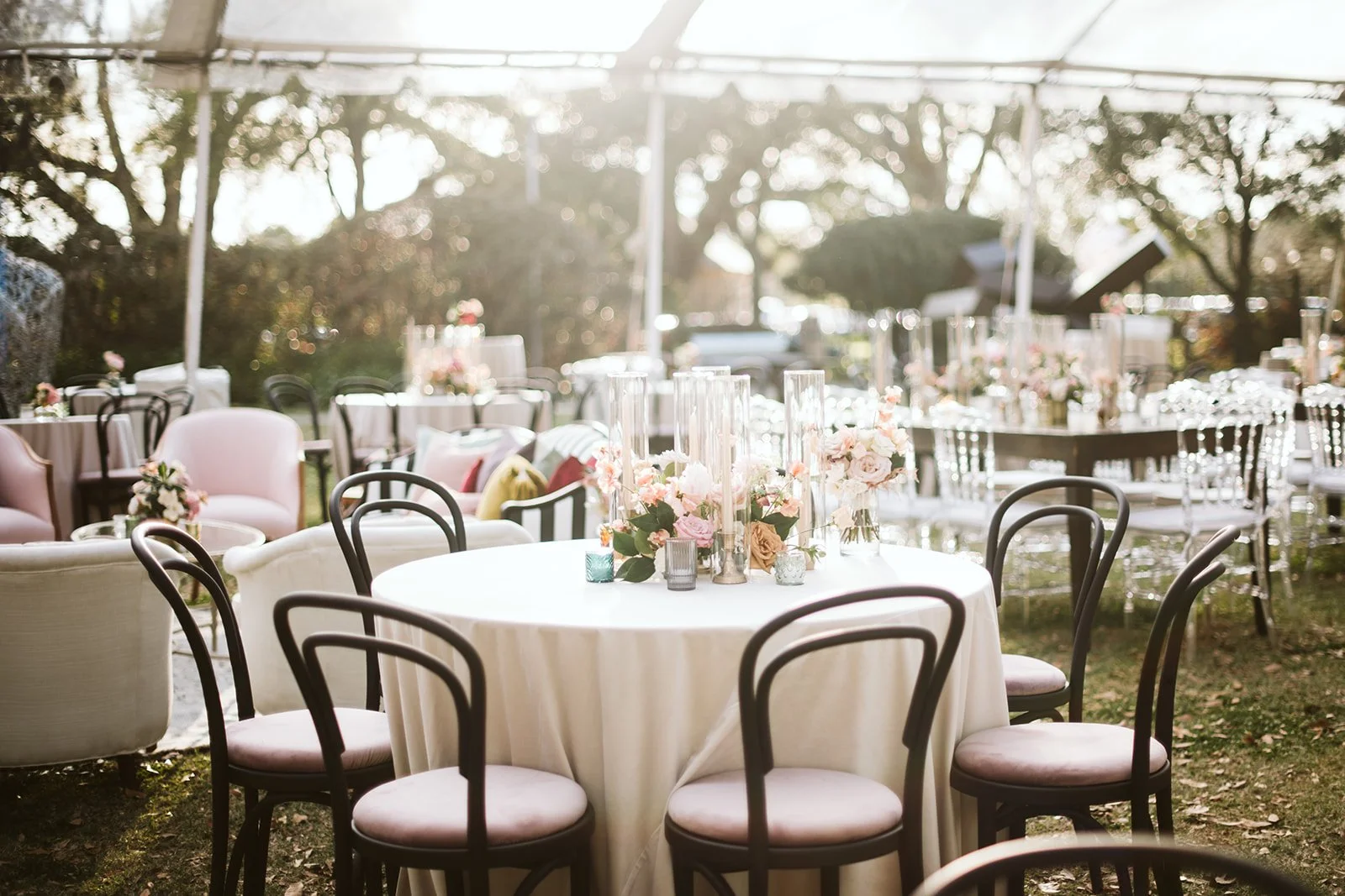 Decorated outdoor event space with round table, floral centerpieces, and chairs, set up for a celebration or wedding.