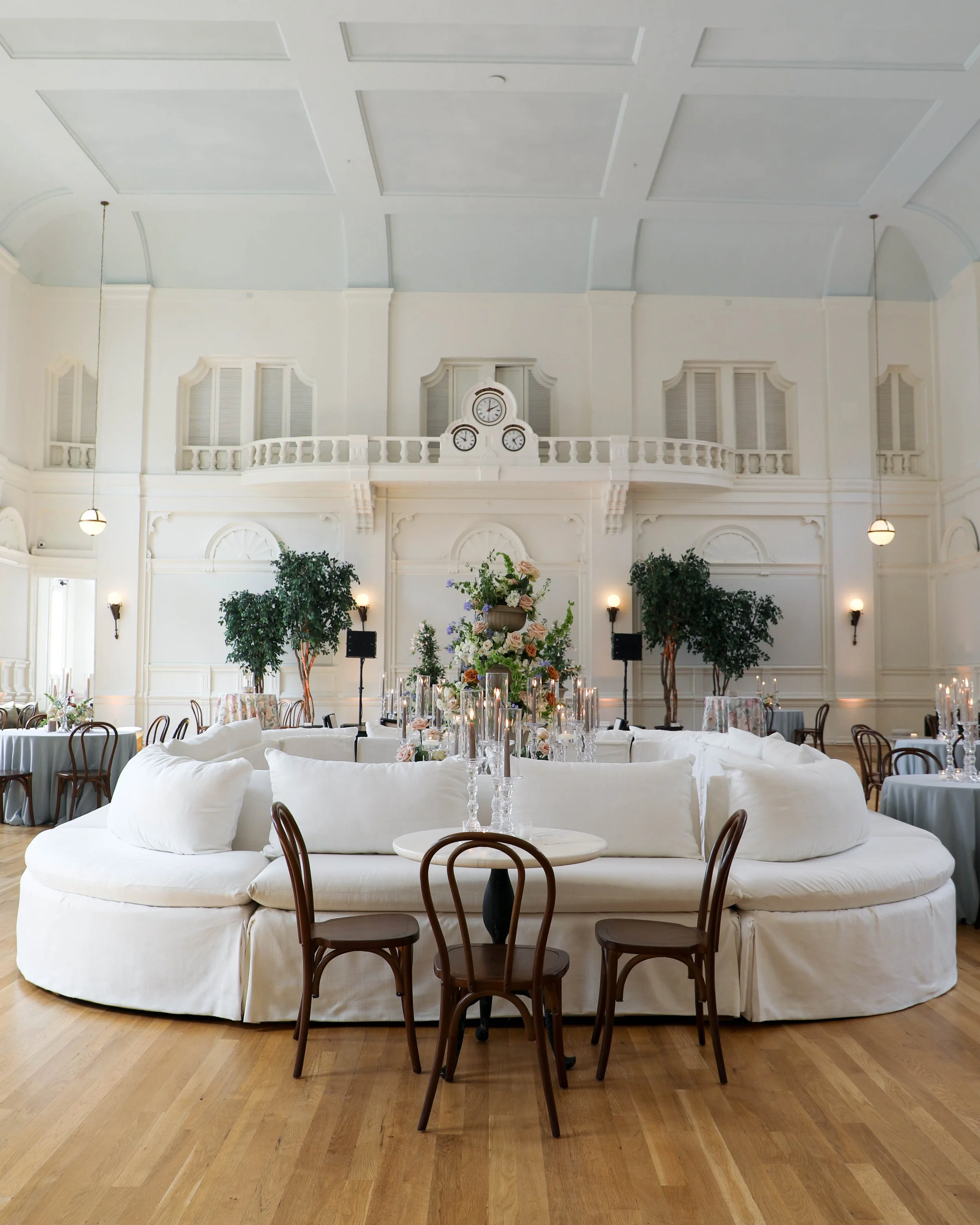 A Wedding reception with white banquettes, round tables with candles, and wooden chairs at the New Orleans Board of Trade.