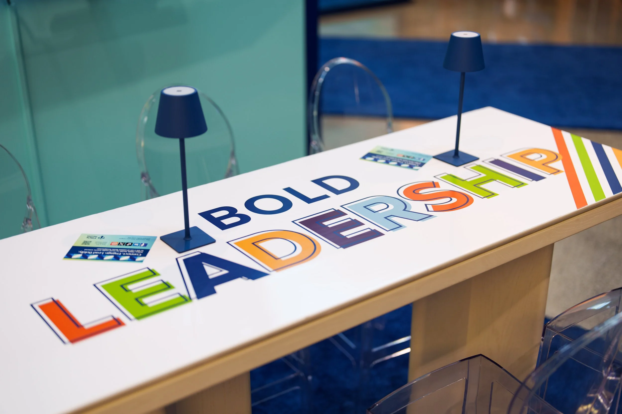 Colorful sign on a table with the words 'BUILDERS LEADERSHIP' in bold, multicolored letters, with two small blue lamps and event tickets nearby.