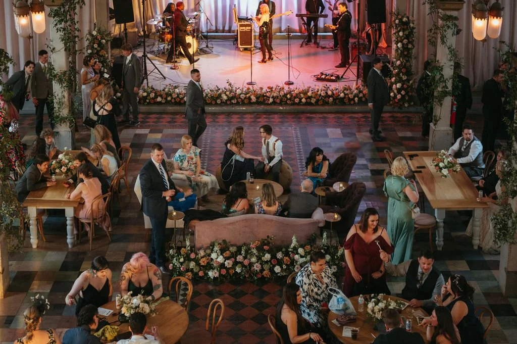 People socializing and dancing at a wedding reception with a band performing on stage in the background.