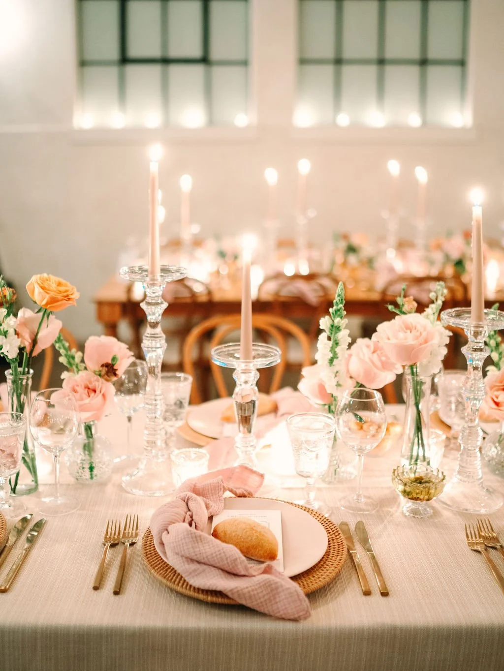 A decorated dining table with pink flowers, tall candles, and glassware for an elegant event