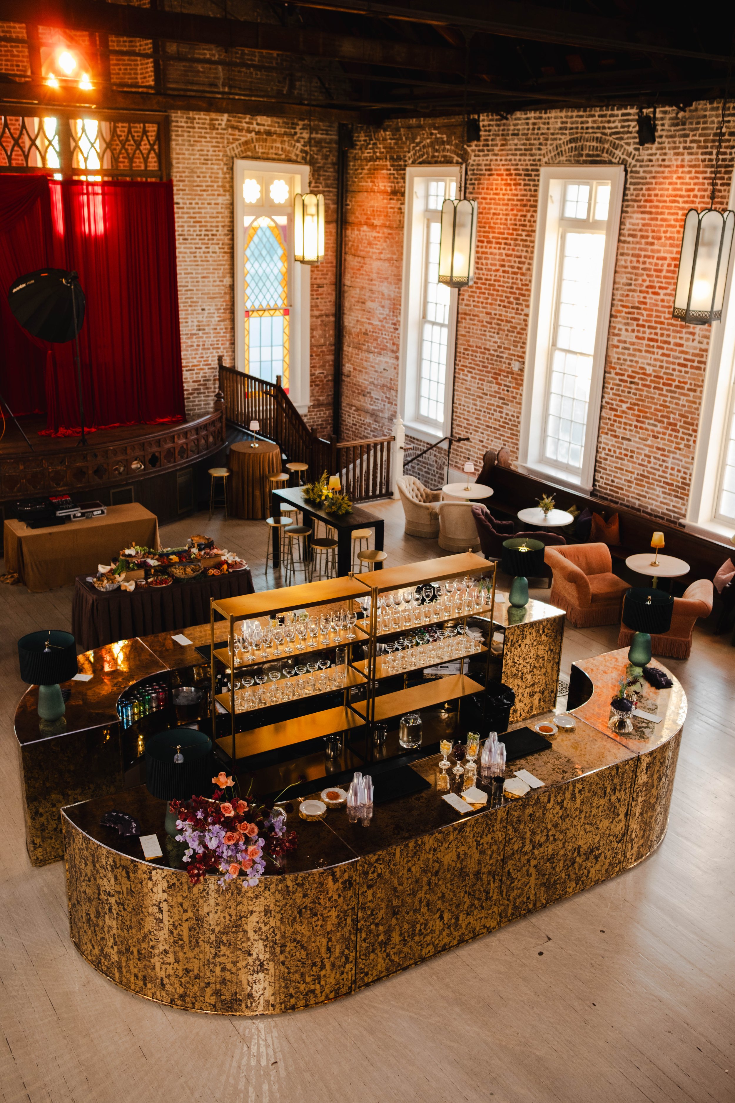 A wedding reception design with a large gold mirrored bar, gold barbacks, lighting, lounge seating with cabarets, pub tables, and barstools at Felicity Church in New Orleans.