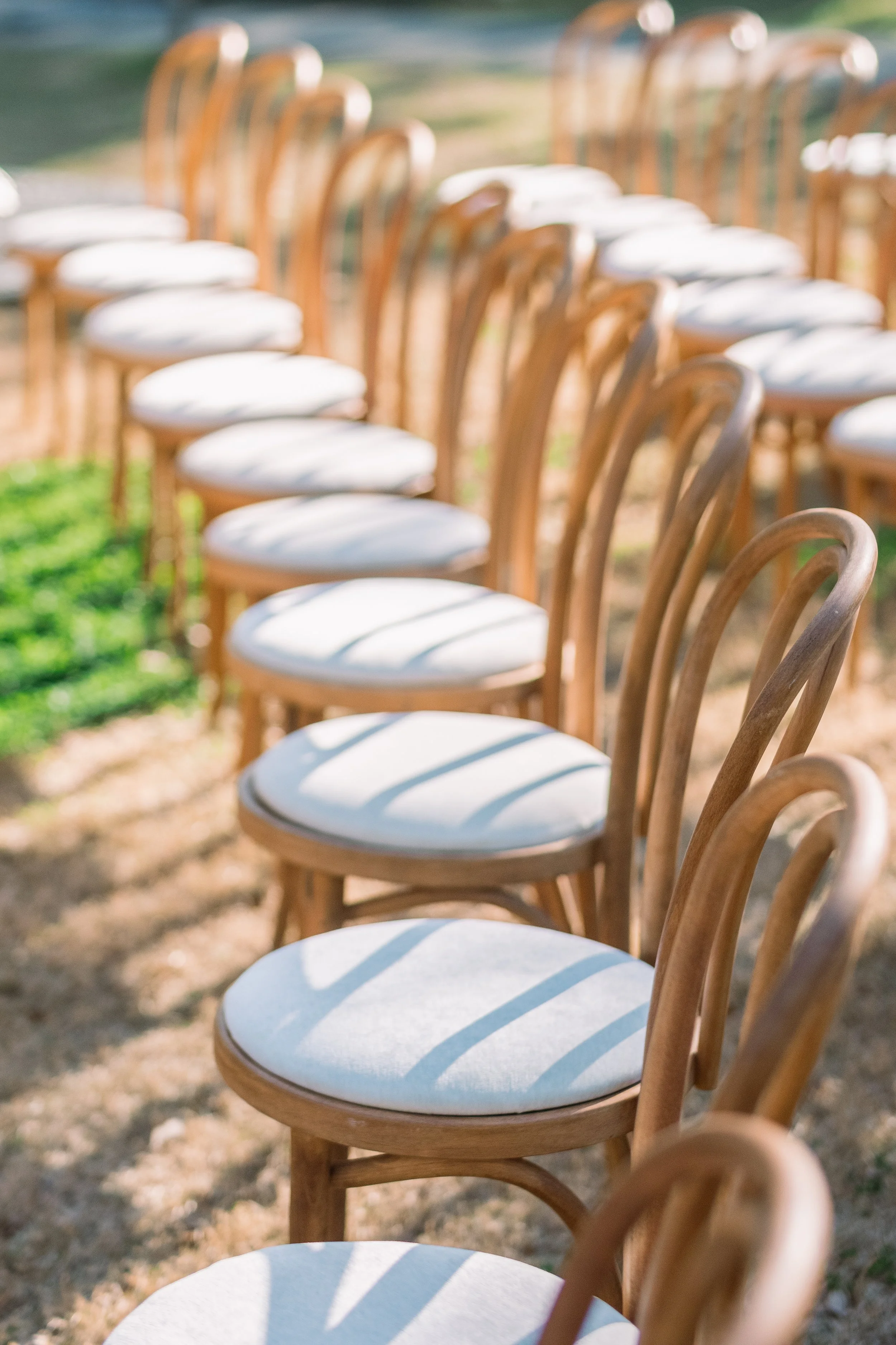 Row of wooden chairs with white cushions outdoors on grass