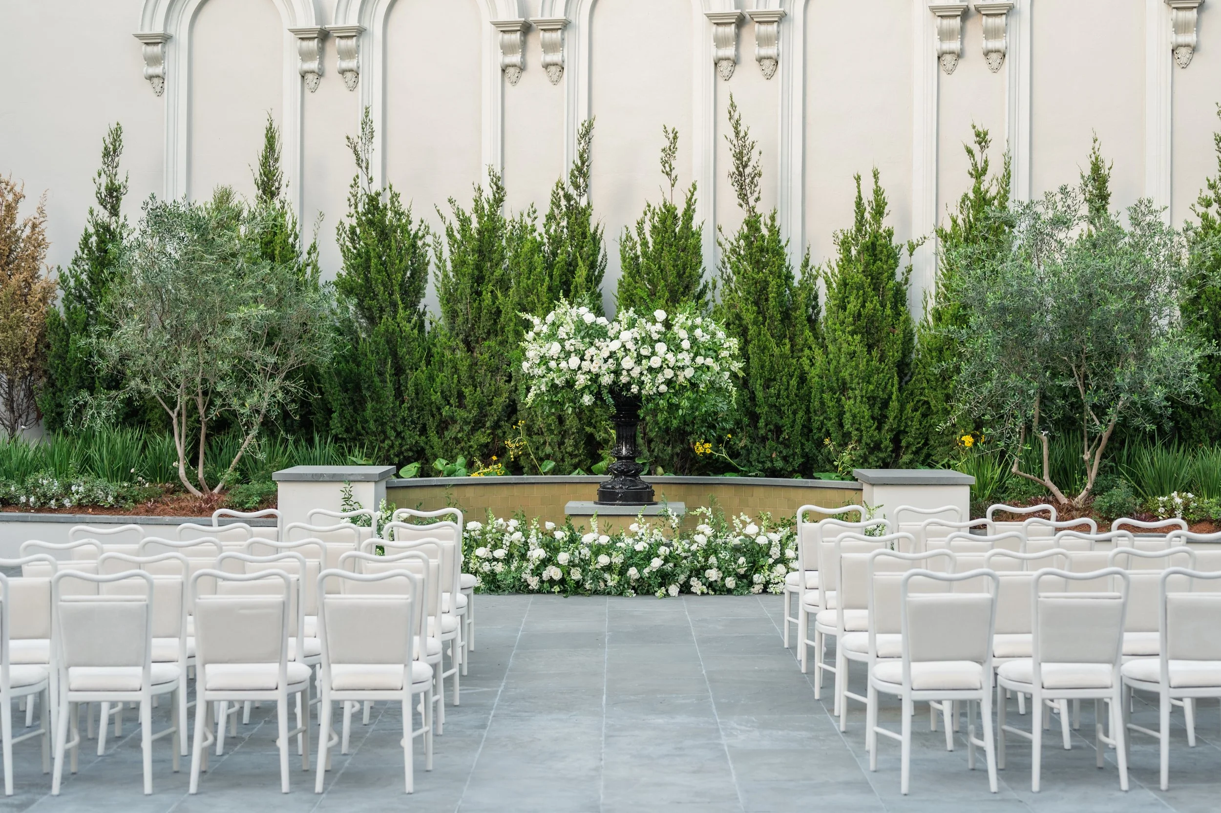An outdoor wedding ceremony with white dining chairs in the courtyard of the New Orleans Board of Trade. 