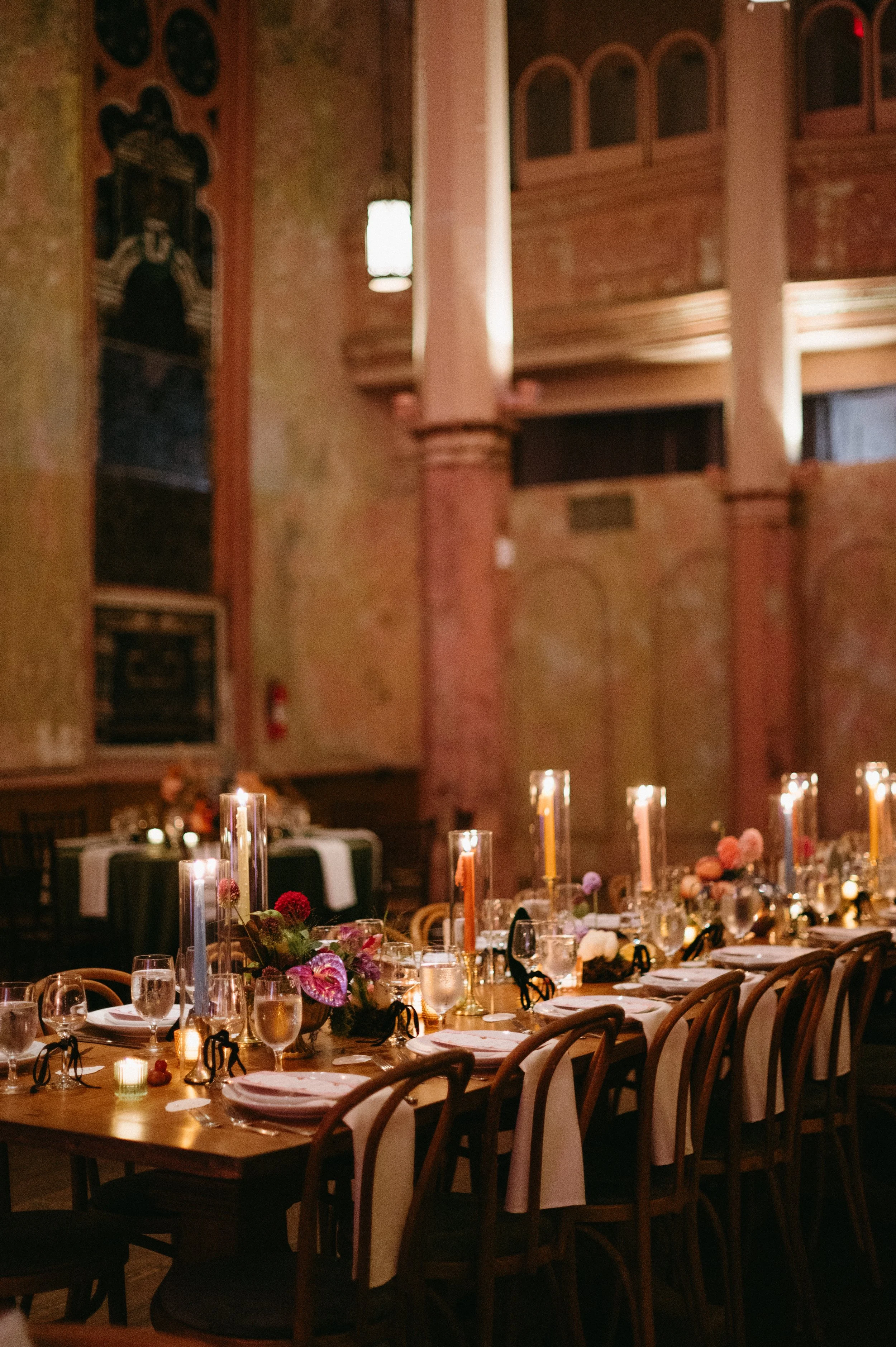 Empty wedding reception hall with decorated tables, floral centerpieces, candles, and dim lighting.