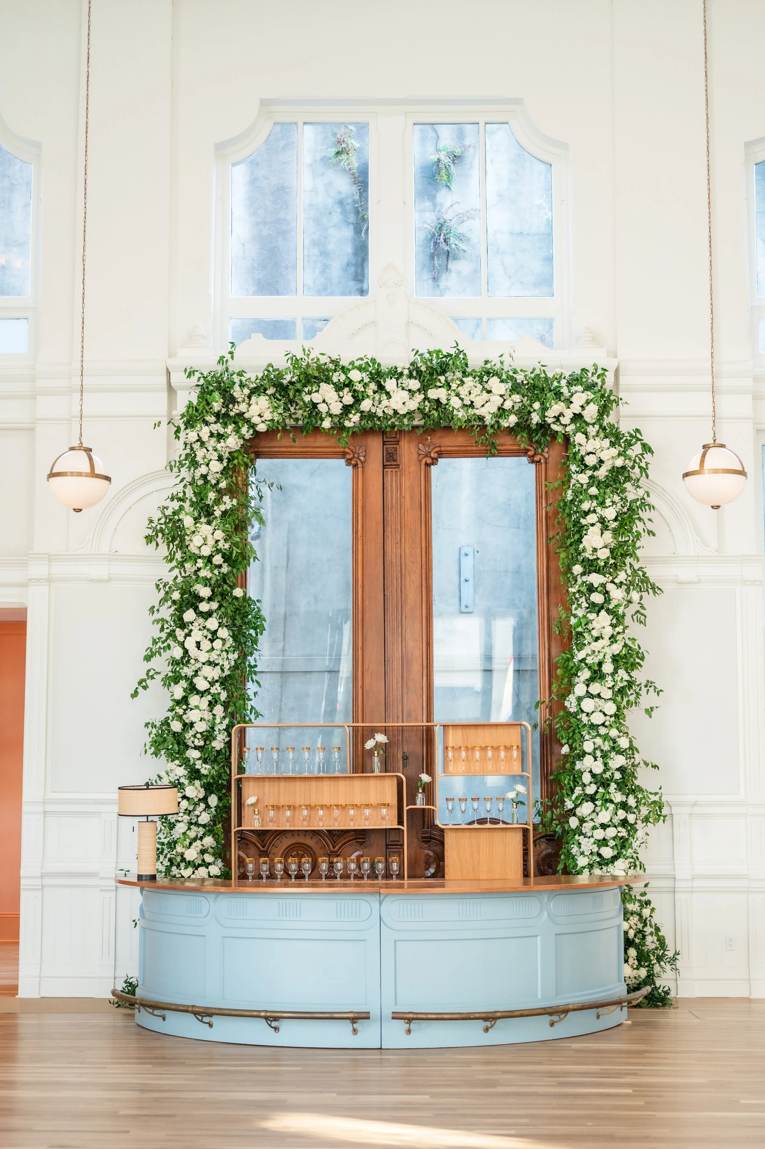 A Wedding reception bar design with a oak wood bar back, a pastel blue round bar with a table lamp on the end of the bar at the New Orleans Board of Trade.