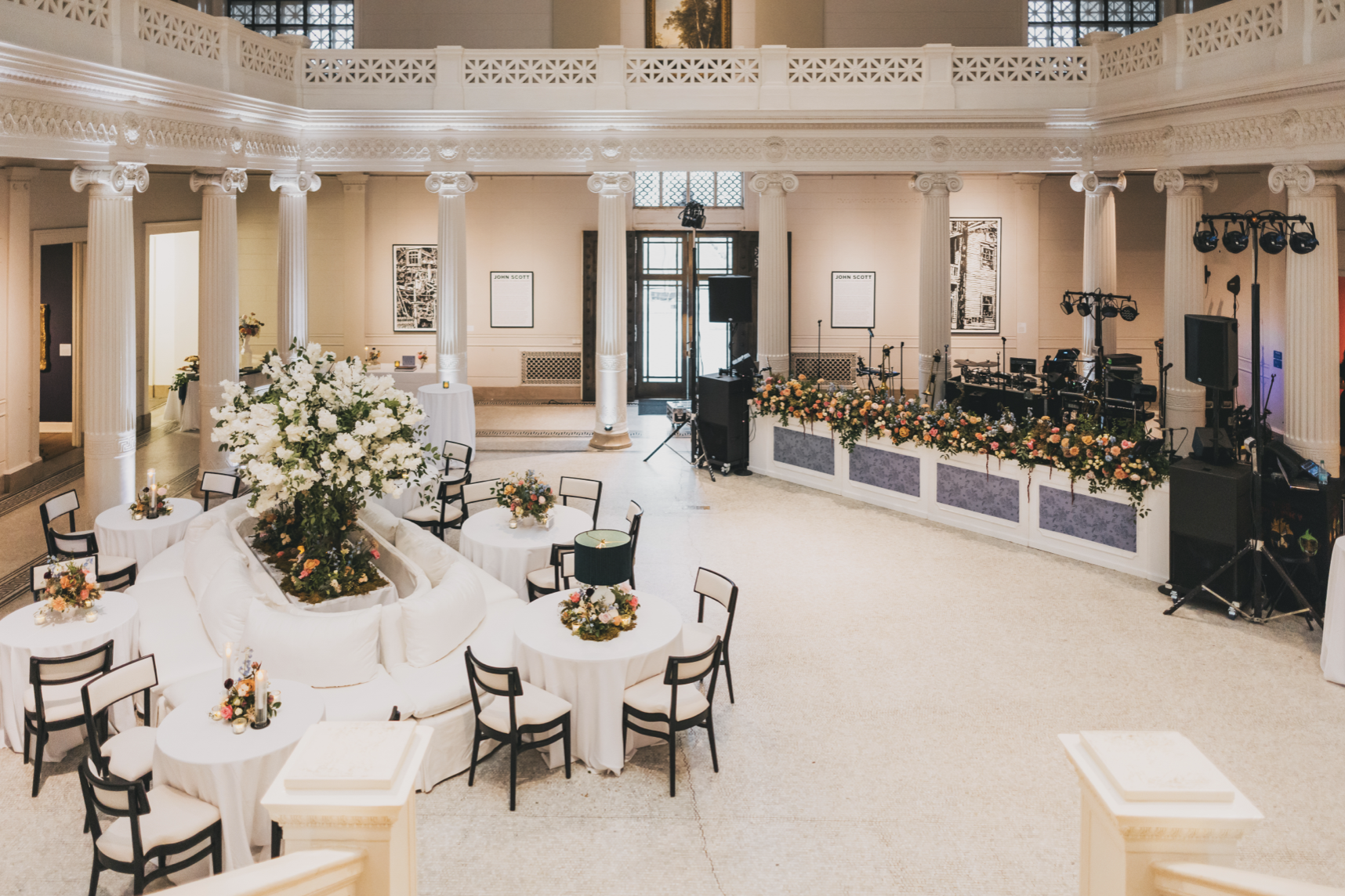Elegant event space with white columns, floral arrangements, and a stage with musical instruments and lighting equipment.