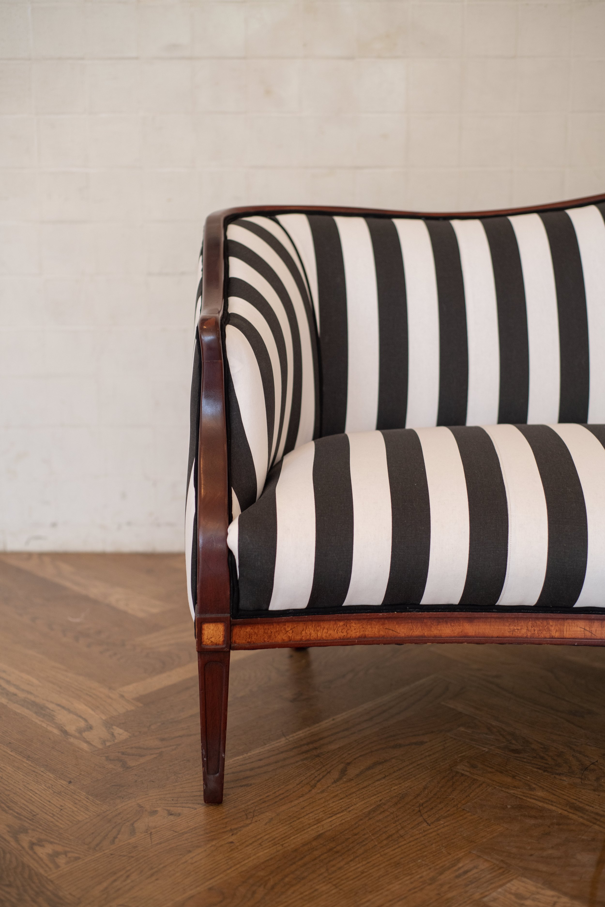 A vintage wooden armchair with black and white striped upholstery, positioned on a wooden floor against a white brick wall.