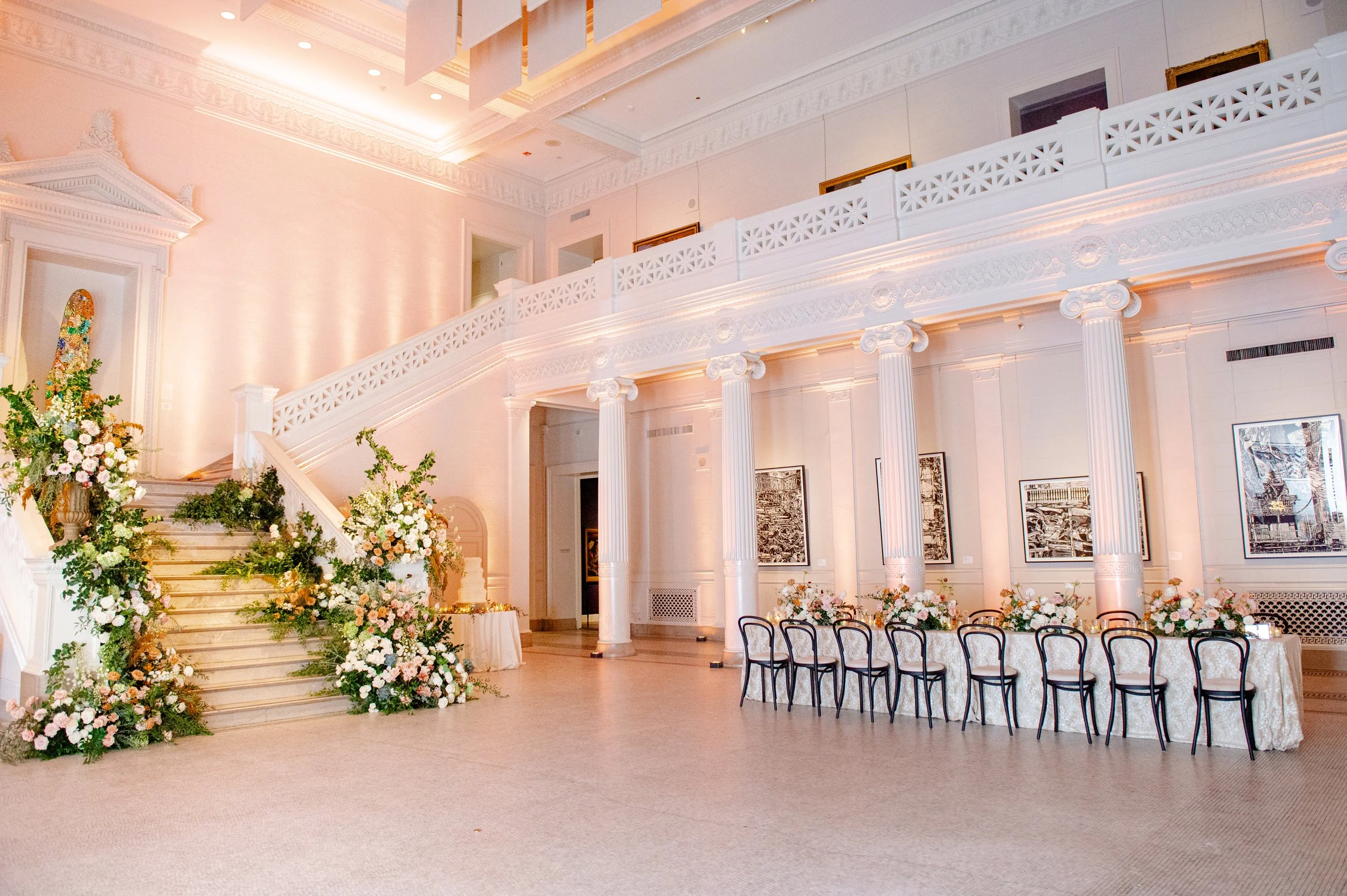 Elegant event venue decorated with flowers, large staircase, and classical columns, set up for a ceremony or reception.