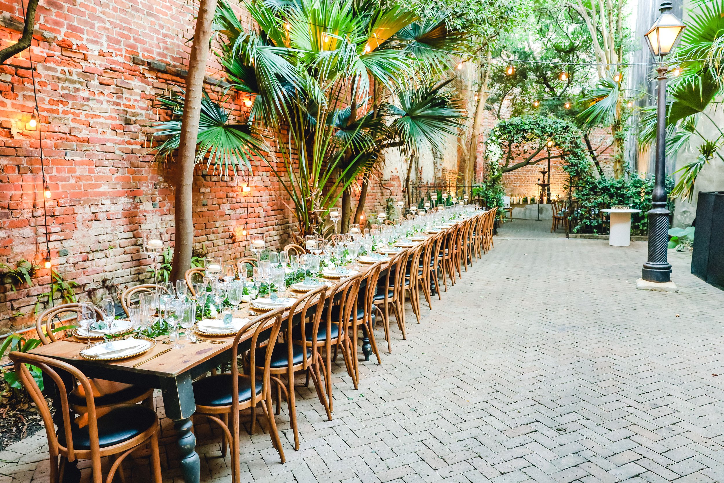 Outdoor seated dinner wedding reception with a long wooden dining tables and dining chairs at the New Orleans Pharmacy Museum.