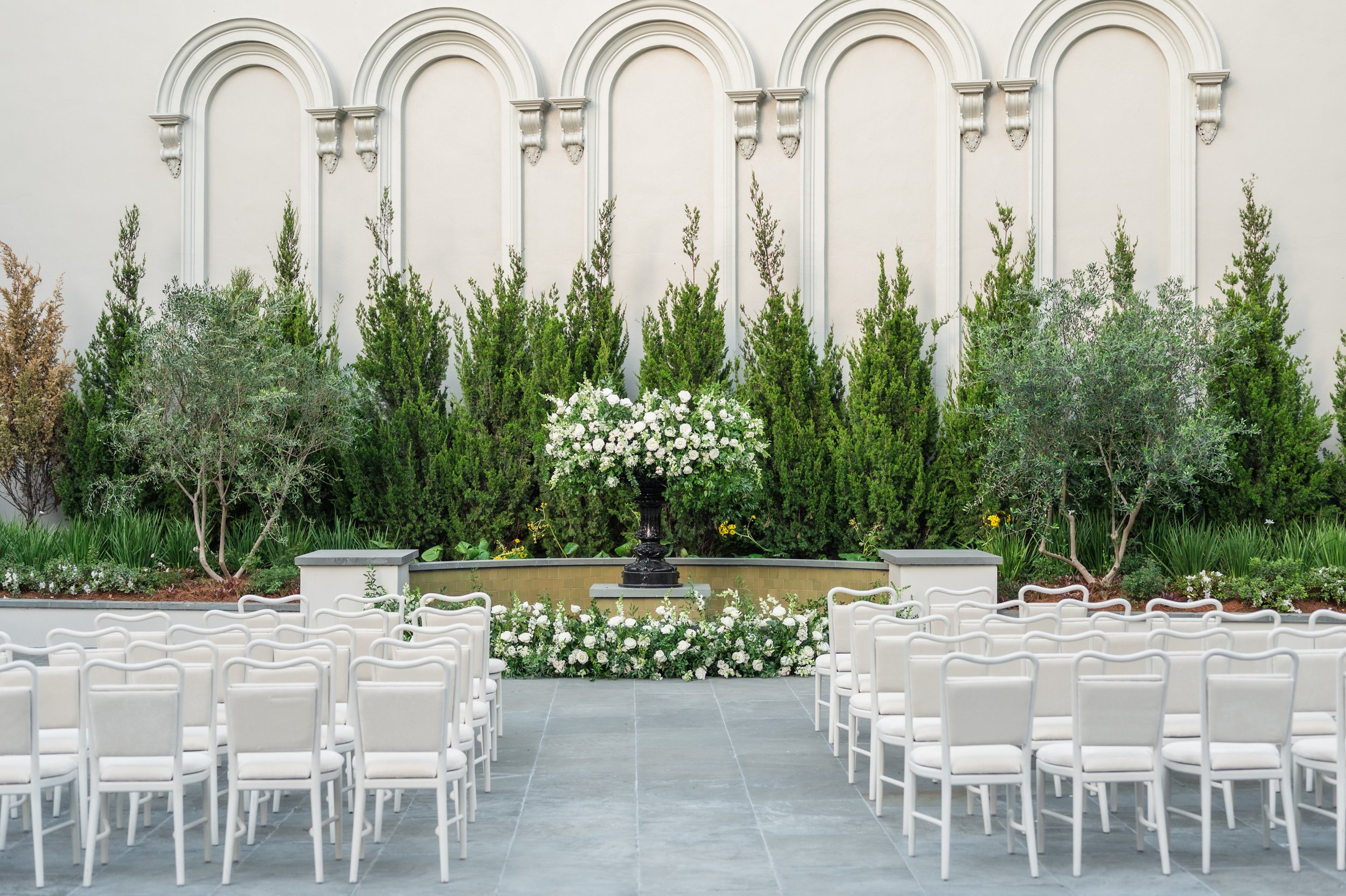 A courtyard wedding ceremony with white dining chairs at the New Orleans Board of Trade.