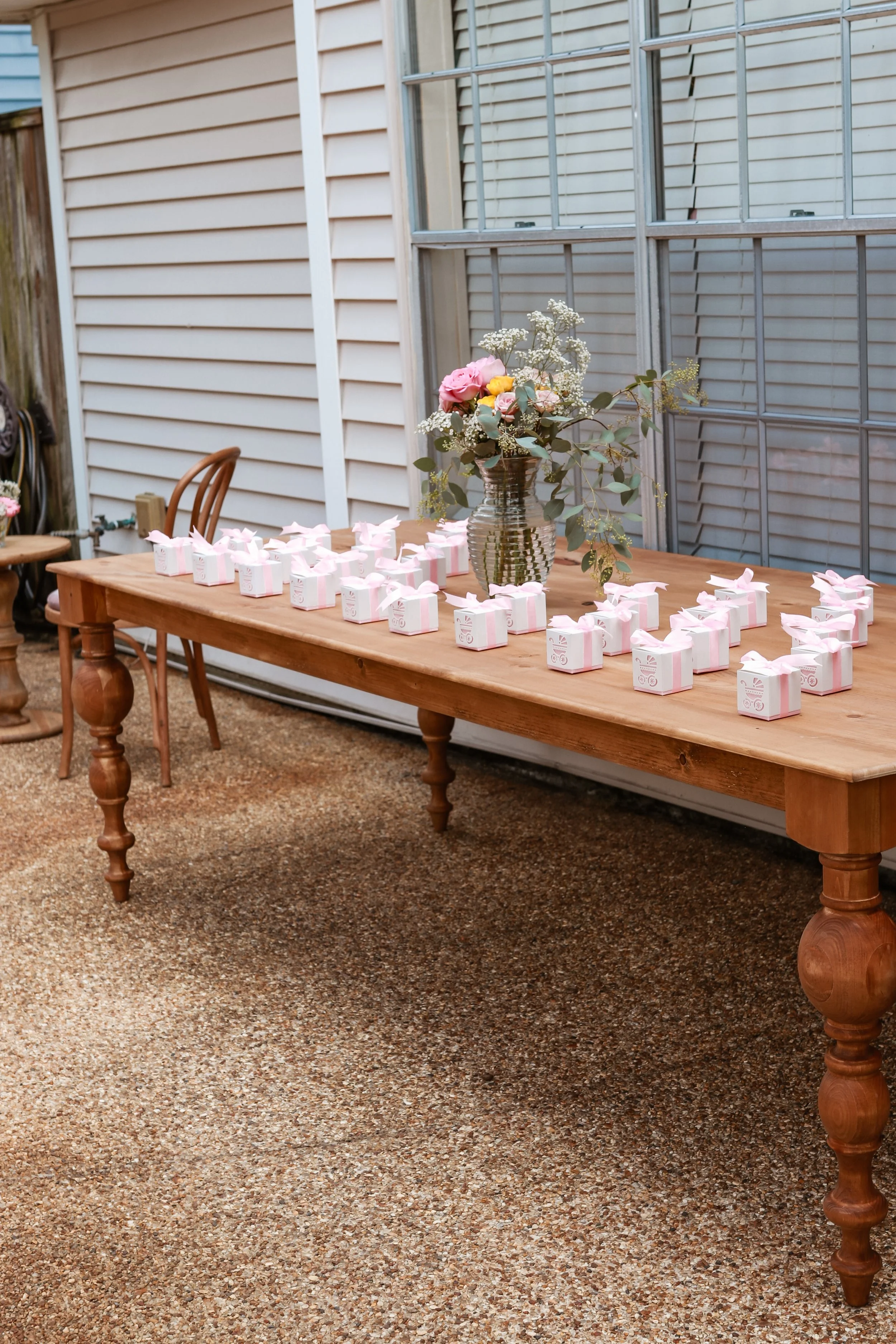 Wooden table with small wrapped gifts and a flower arrangement in a glass vase in an outdoor patio area.