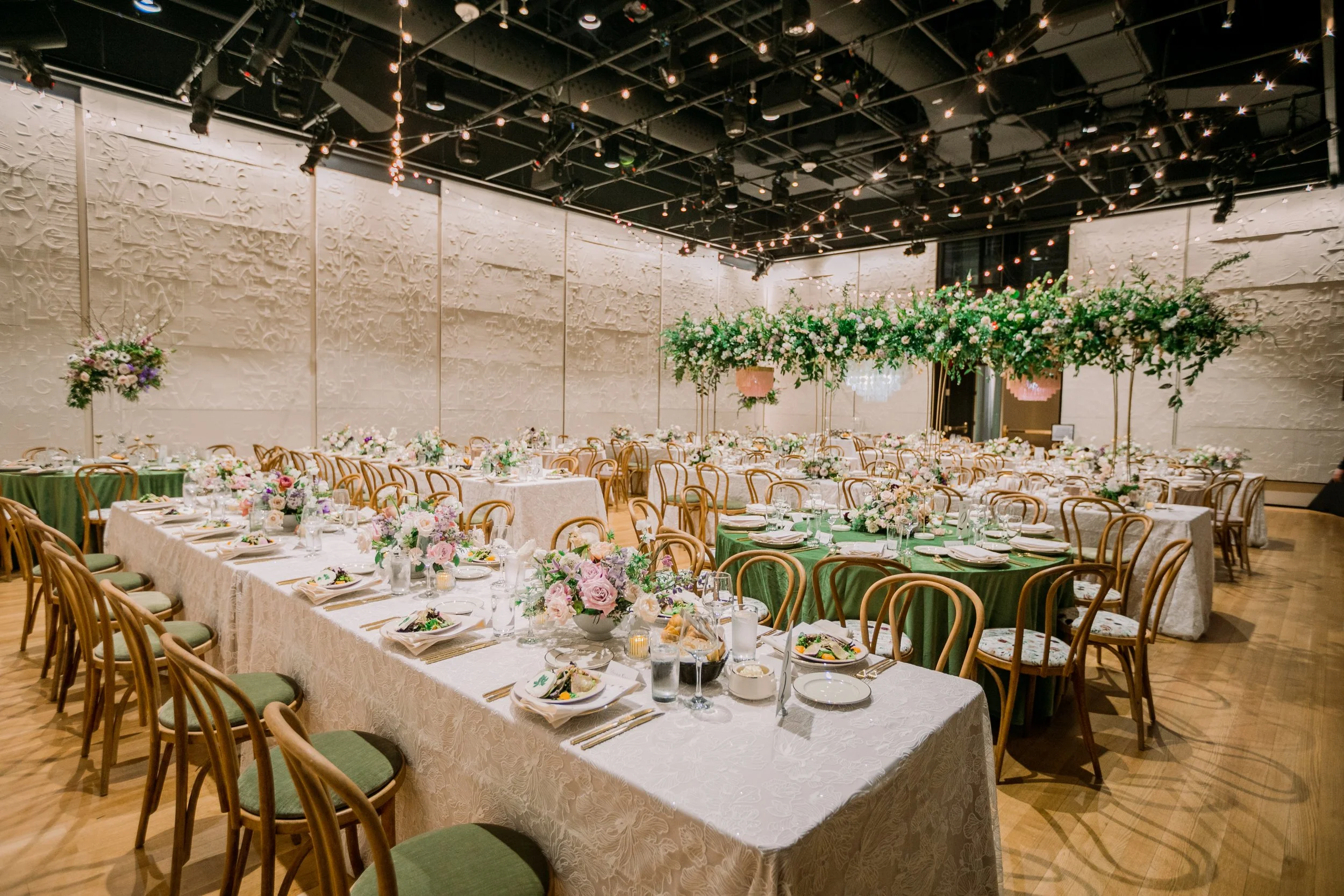 Elegant event hall decorated with floral arrangements, tables with white lace tablecloths, and string lights hanging from the ceiling.