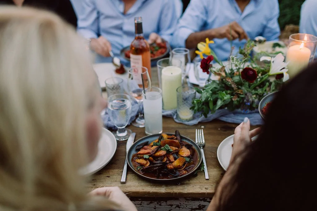 A family dinner table with a floral centerpiece, drinks, and a plate of roasted vegetables in the foreground.