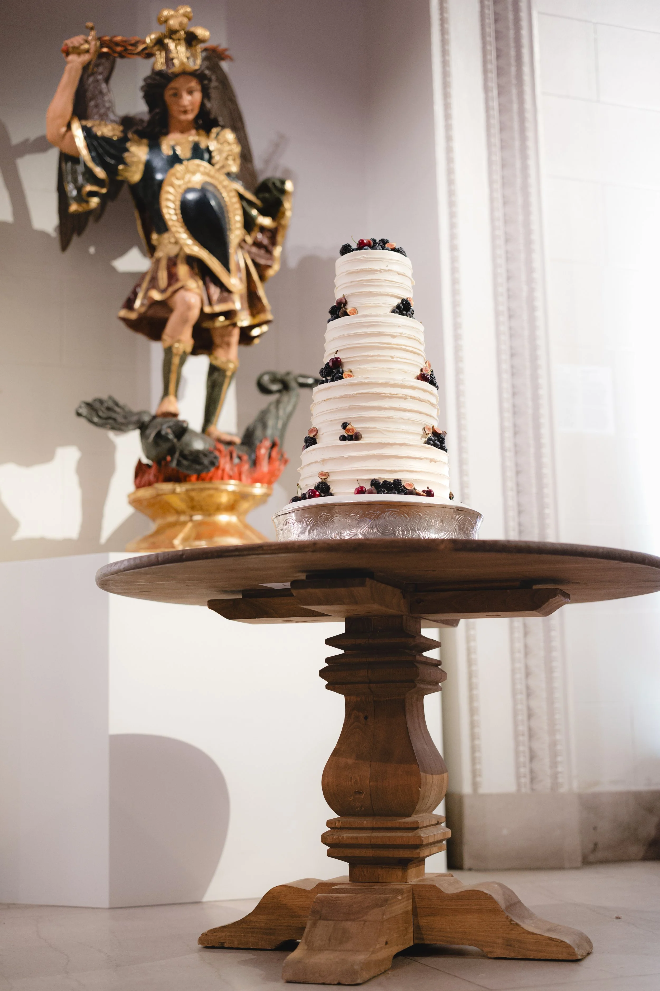 A tall, three-tiered white cake decorated with black and red berries on a wooden table.