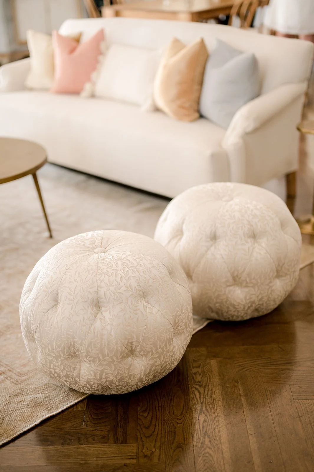 Close-up of two round, upholstered ottomans with a floral pattern in a living room setting.