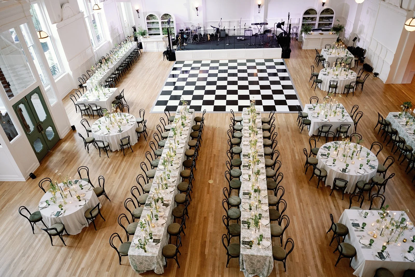 A wedding reception overhead view of a seated dinner with two white bars, with white barbacks, white stage fronts, black dining chairs and mixed round and rectangular dining tables at the New Orleans Board of Trade. 