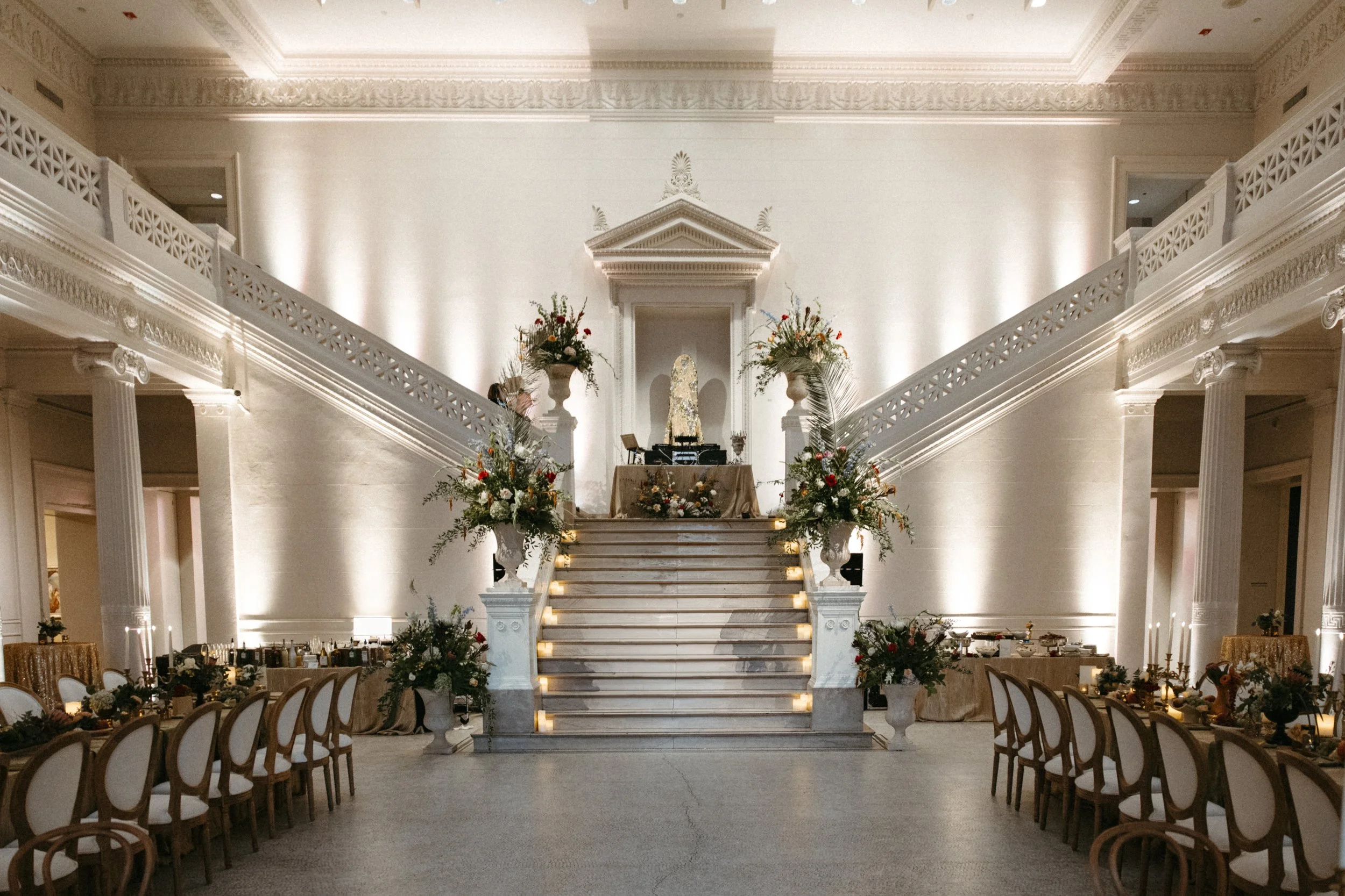 Elegant indoor wedding ceremony setup with a grand staircase, floral arrangements, and dining tables decorated for guests.