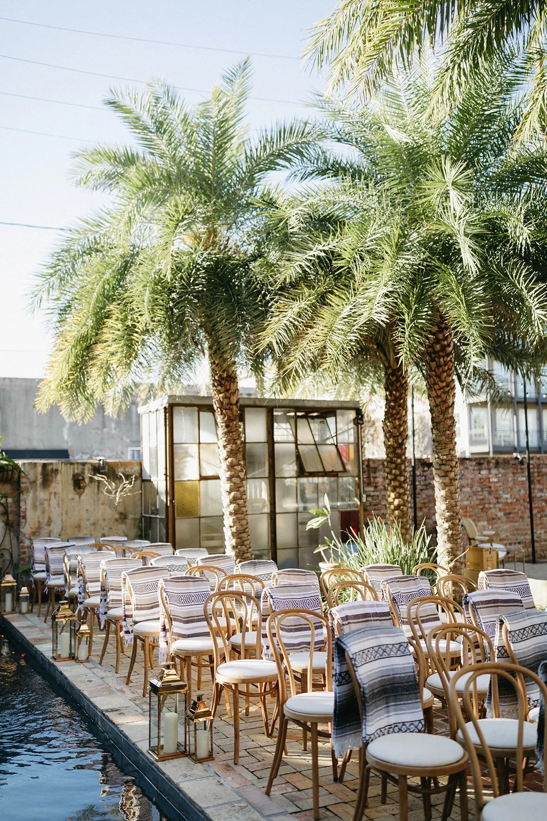 Outdoor seating area with wooden chairs and striped towels near a pool, surrounded by tall palm trees.