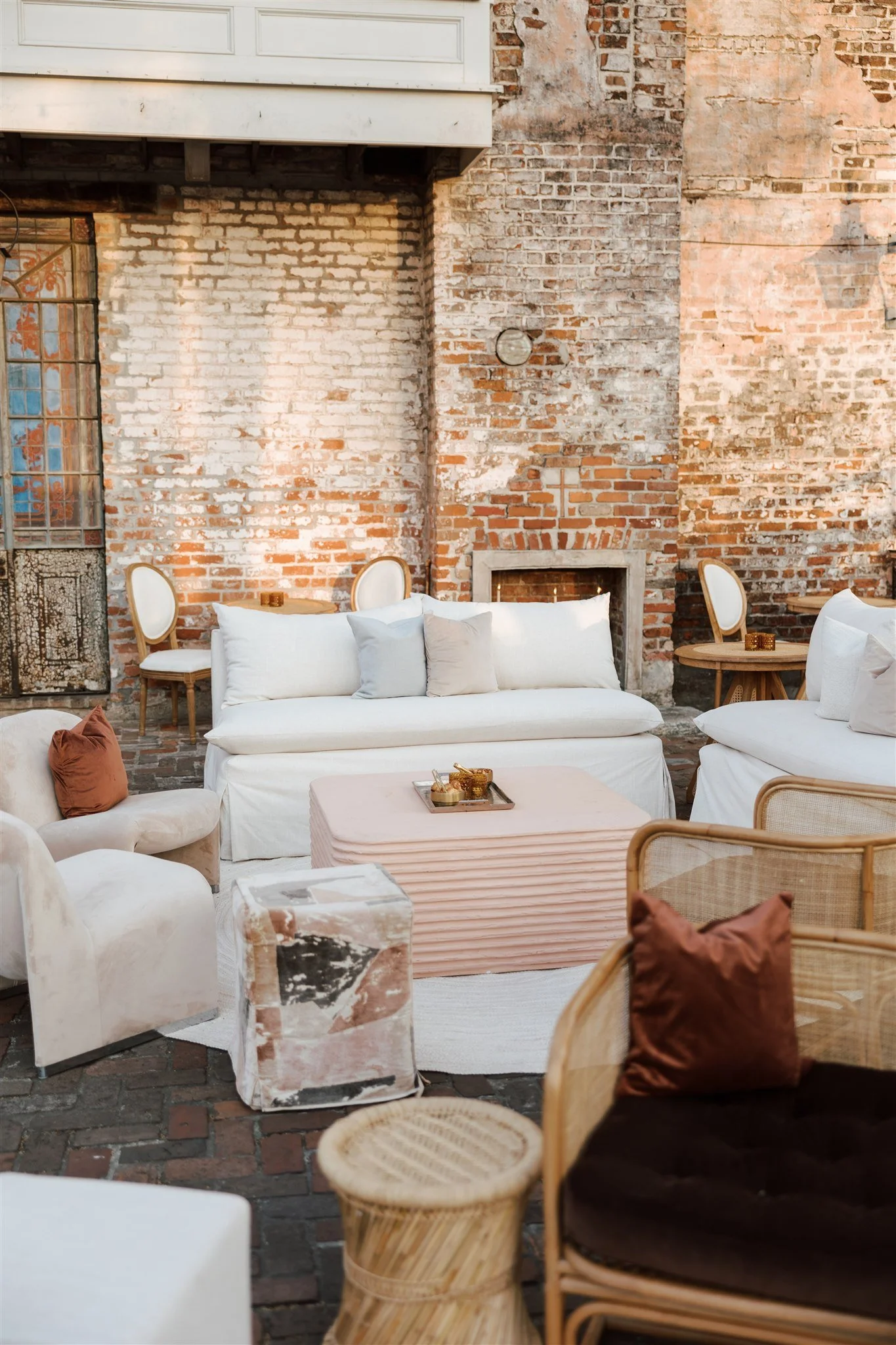 Indoor seating area with a brick wall, white sofas, wooden chairs, and tables, in a rustic or vintage style.