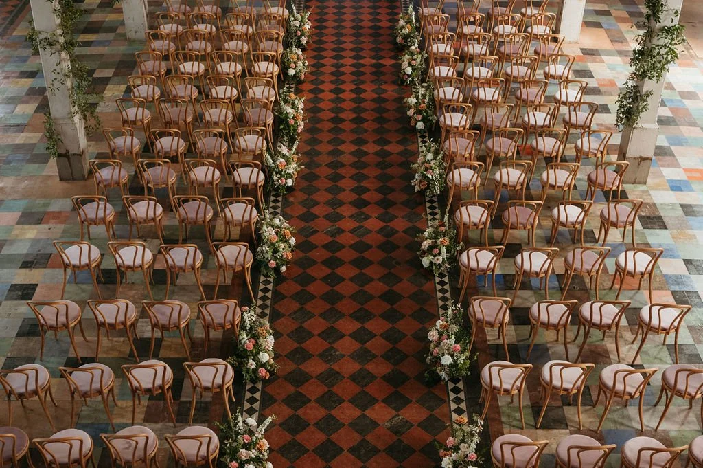 Empty chairs arranged in rows along a floral decorated aisle for a wedding or event.