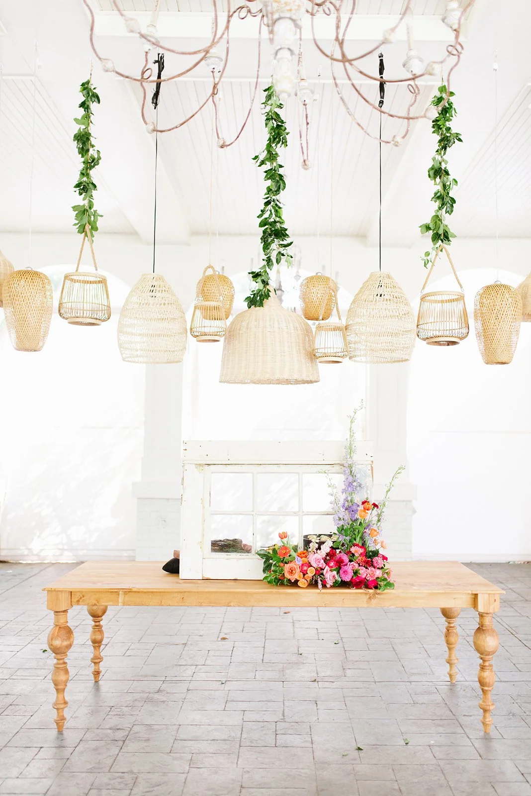 A decorative display with hanging wicker lamps, green hanging plants, and a wooden table with a floral arrangement, set against a white background in a bright room.