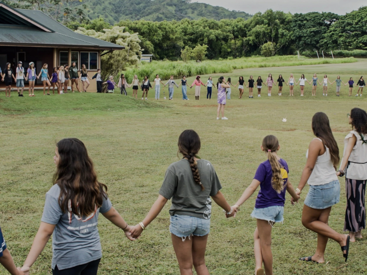 Middle-school students hold hands in a big circle on the school grounds.