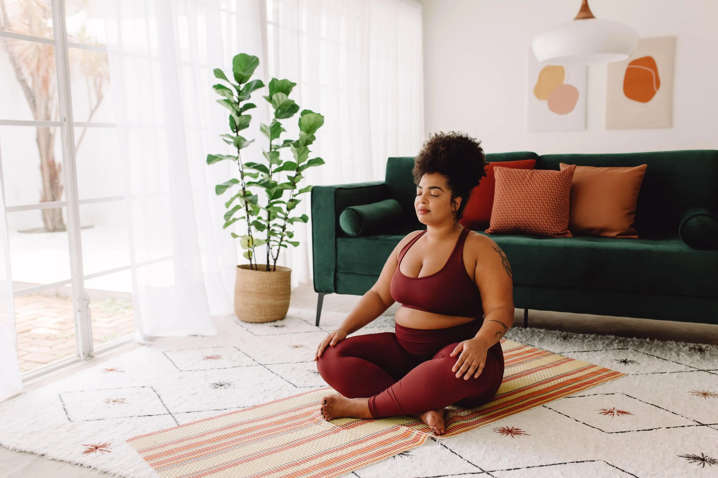 BIPOC person sitting cross-legged on mat meditating.