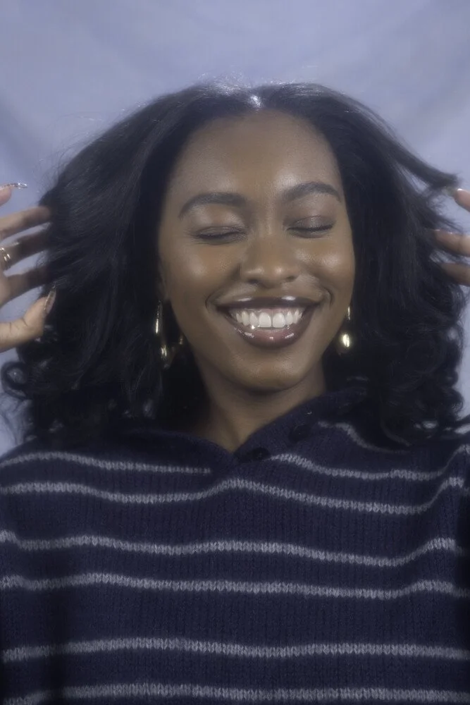 Shantae Howell smiling, in a blue and grey striped jumper, in front of a blue background