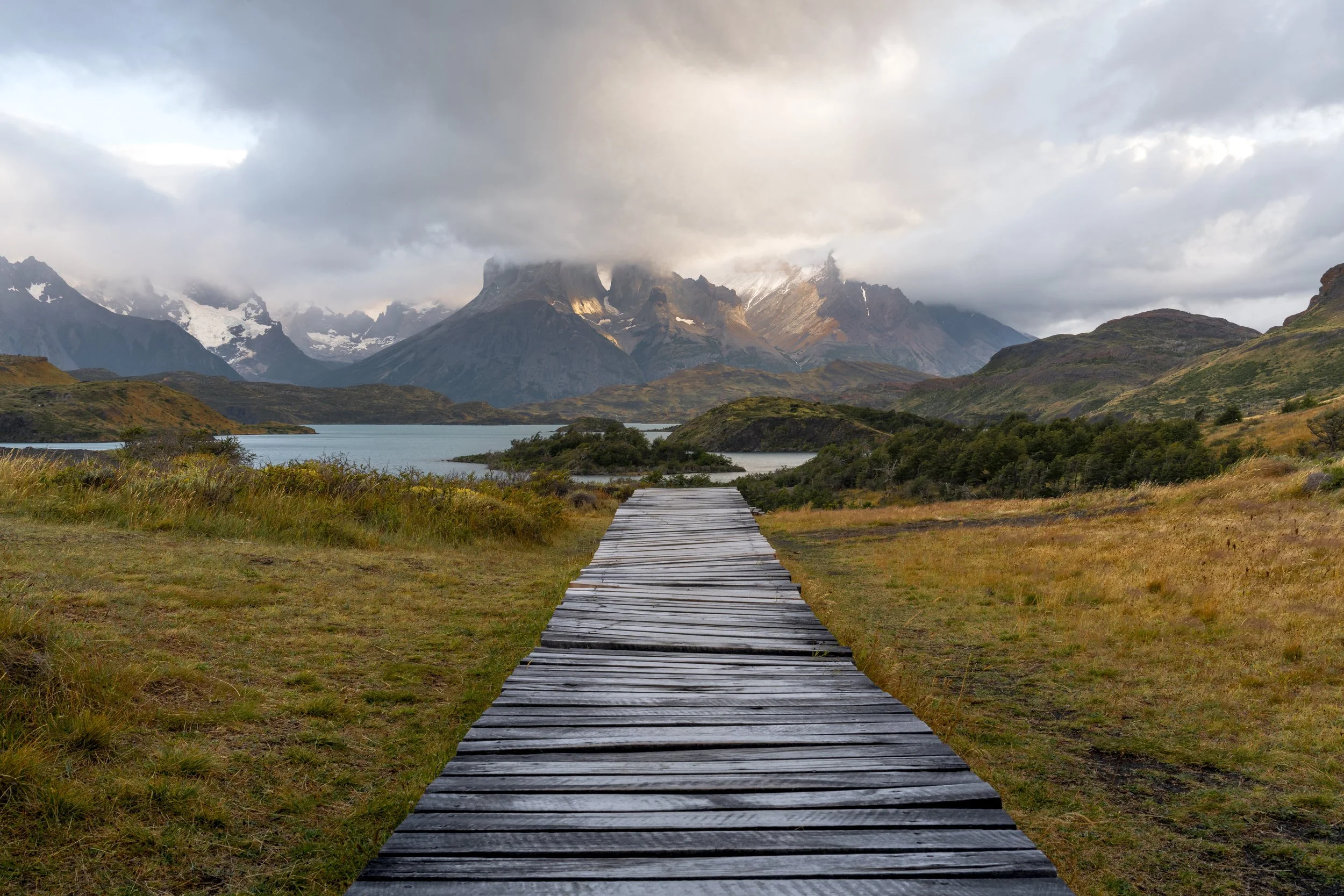 The peaks of torres del paine surrounded by clouds, a wooden walkway leading up from the bottom towards the mountains