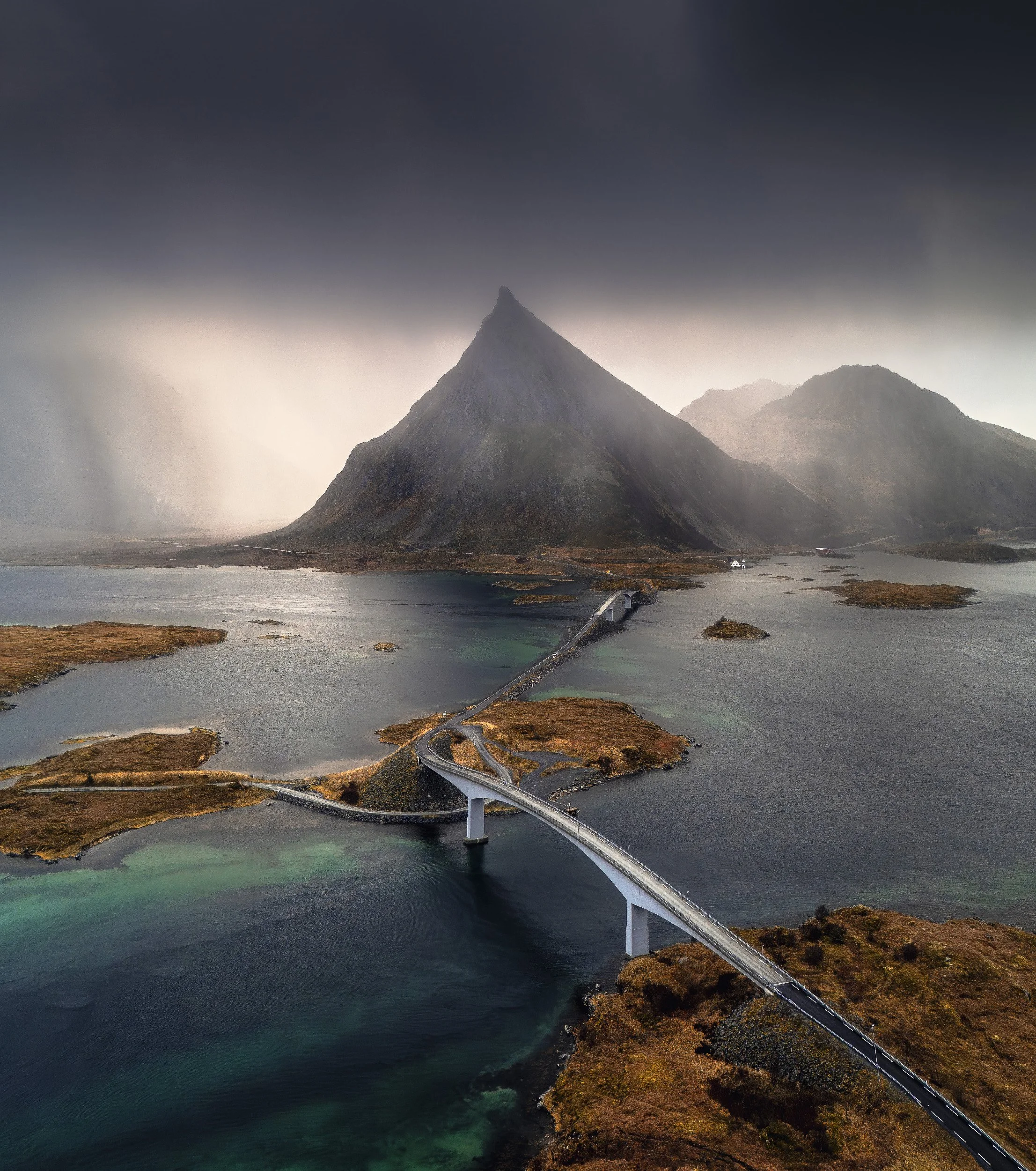 A mountain with a steep, pointed peak surrounded by lakes and a bridge in a scenic landscape.