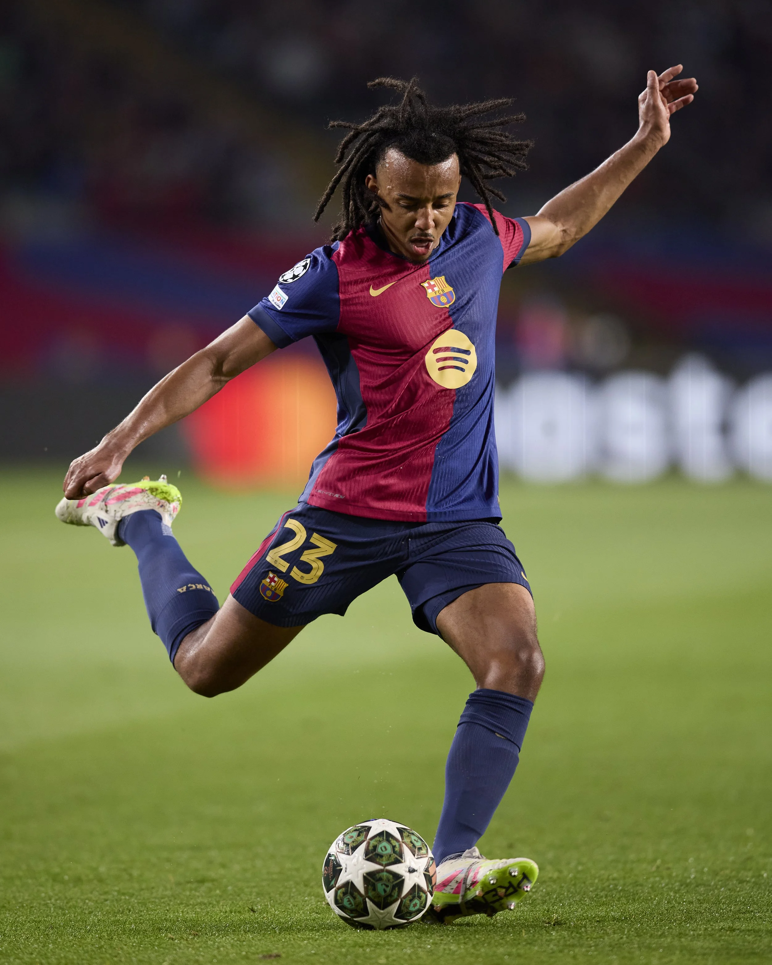 Jugadora de fútbol de Barcelona en acción, con uniforme azul y rojo, controlando el balón en el campo de juego.