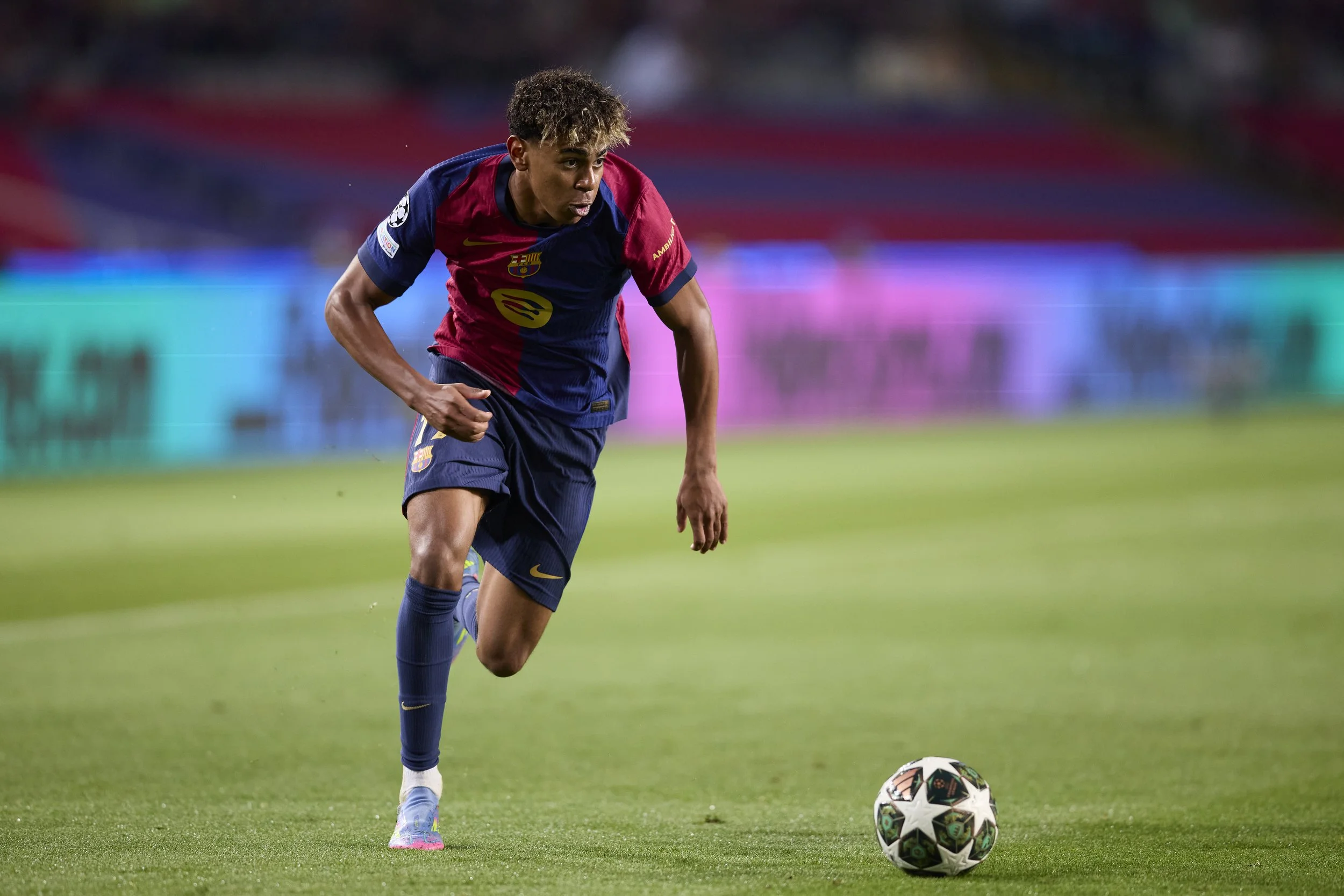 Jugador de fútbol en acción en el campo, vestido con uniforme de FC Barcelona, con el balón en frente durante un partido.
