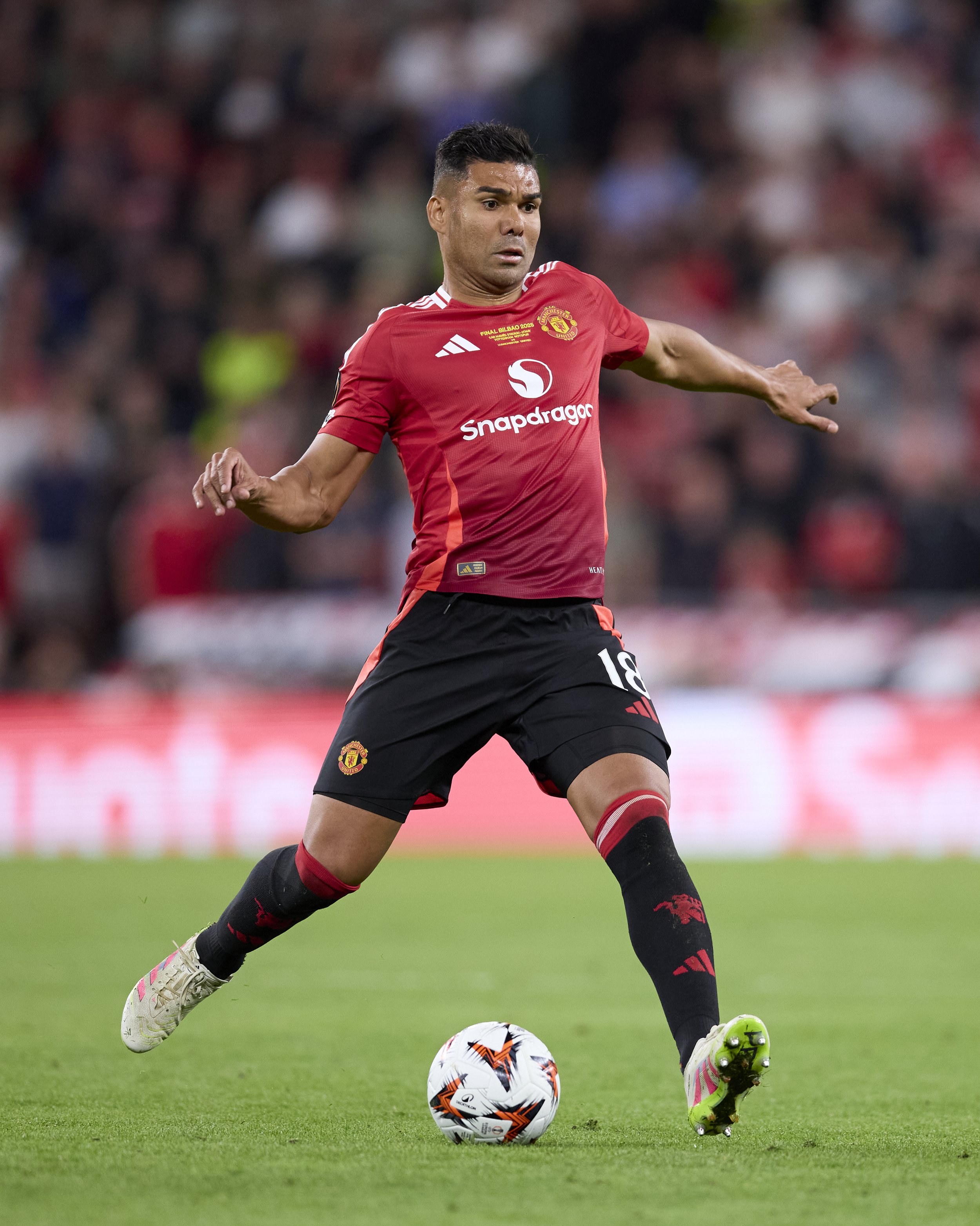 Jugador de fútbol en uniforme rojo y negro, controlando una pelota en el campo durante un partido.