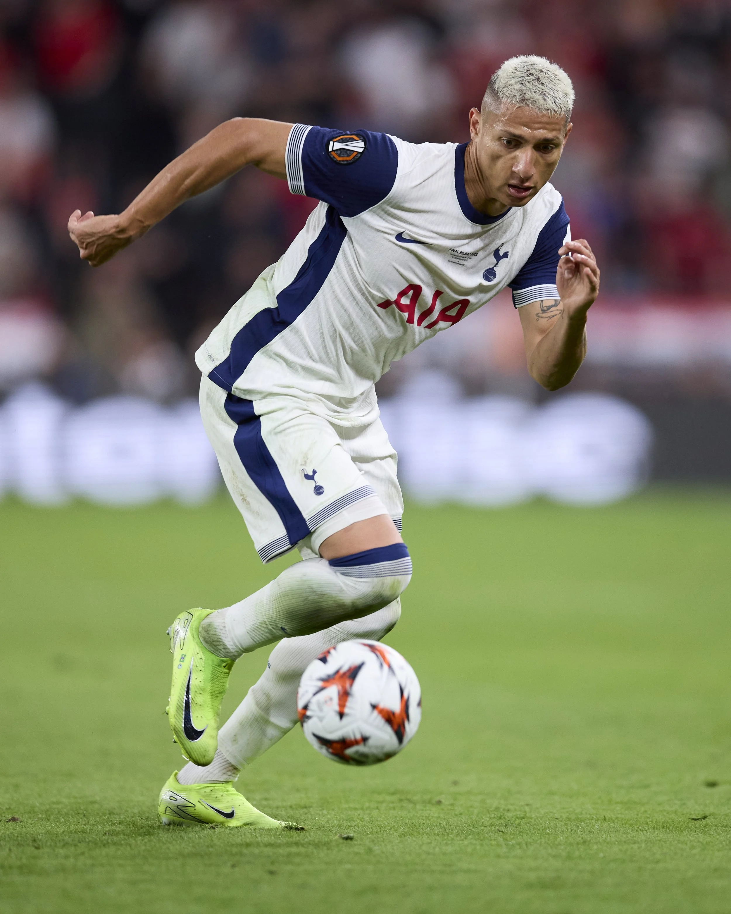 Jugador de fútbol en acción, vestido con uniforme blanco y azul, entrenando en el césped, con balón.