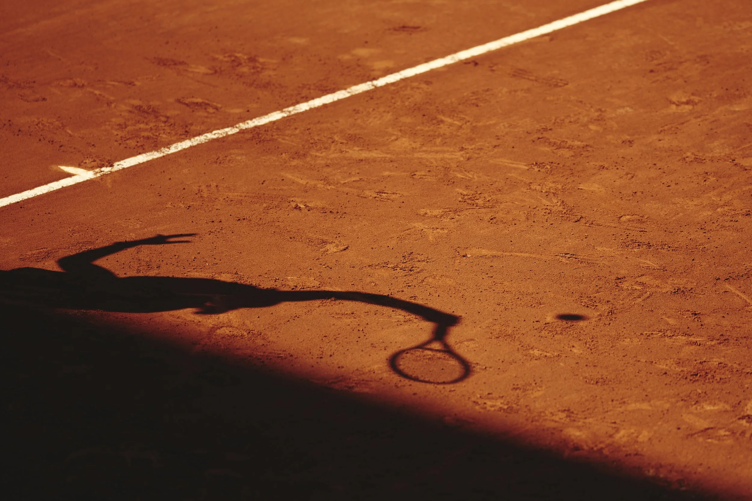 Sombra de una raqueta de tenis y la pelota en una cancha de arcilla.