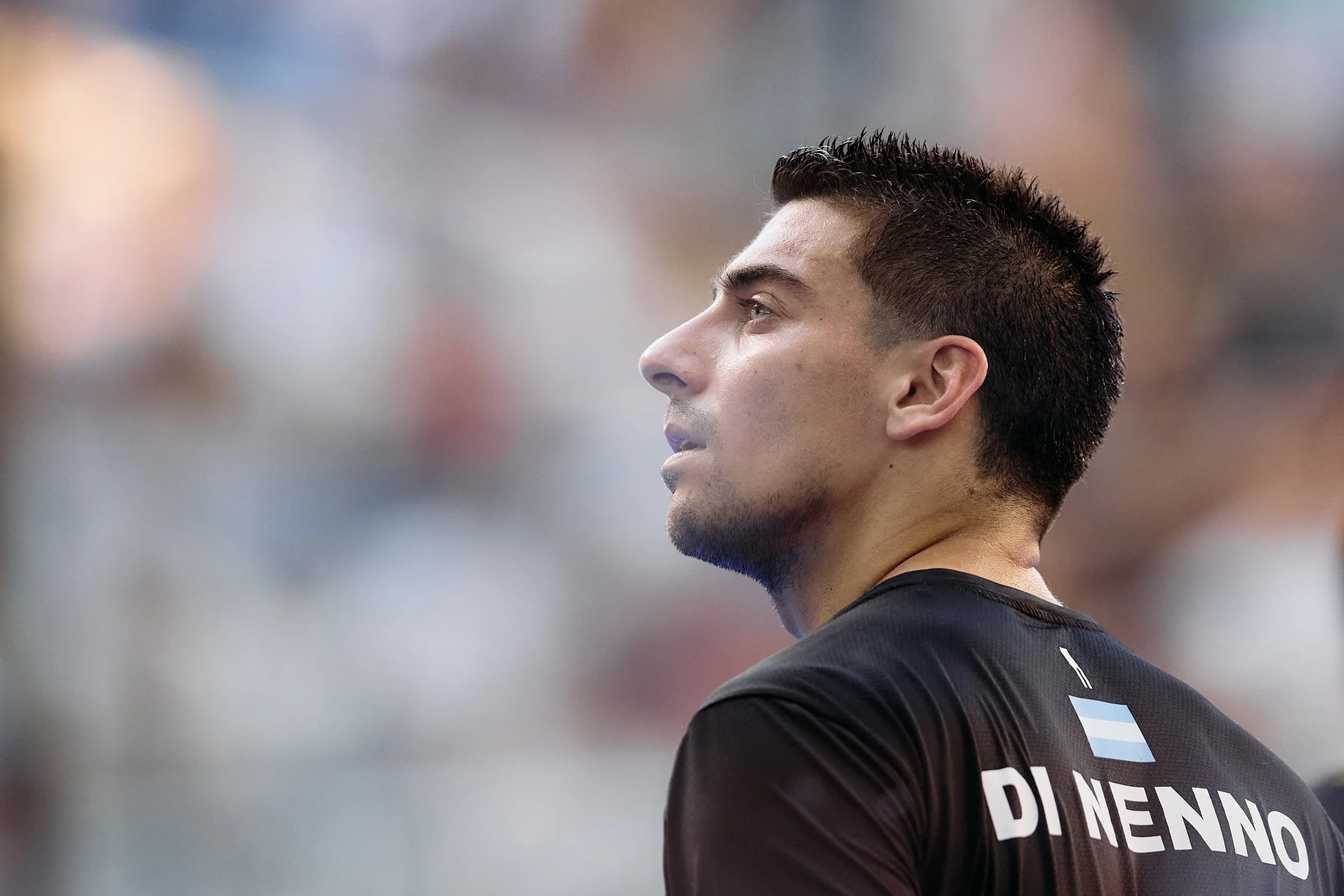 Retrato de un futbolista con camiseta negra, vista de perfil, en un estadio. La camiseta tiene la bandera de Argentina y el nombre Dinenno en la espalda.