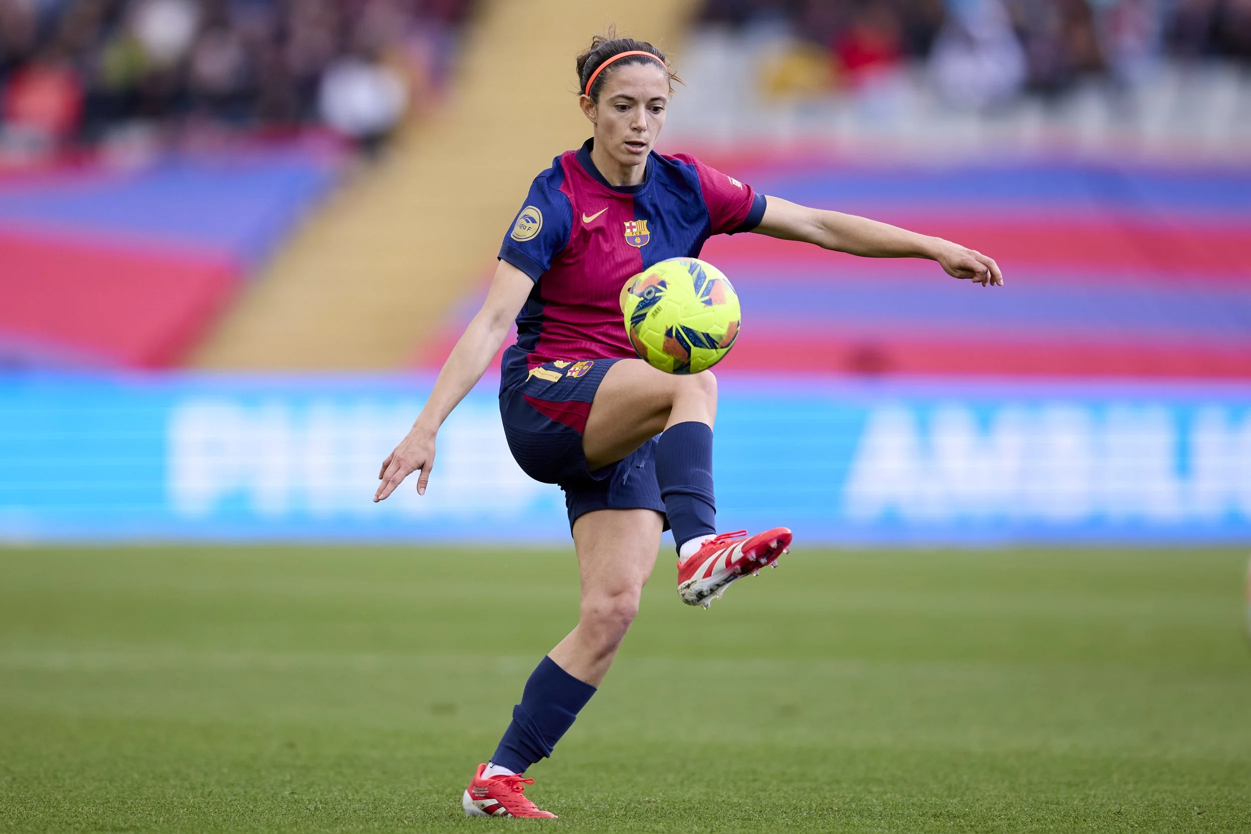 Una jugadora de fútbol en uniforme del FC Barcelona le da una patada a un balón de fútbol en un campo de césped durante un partido.